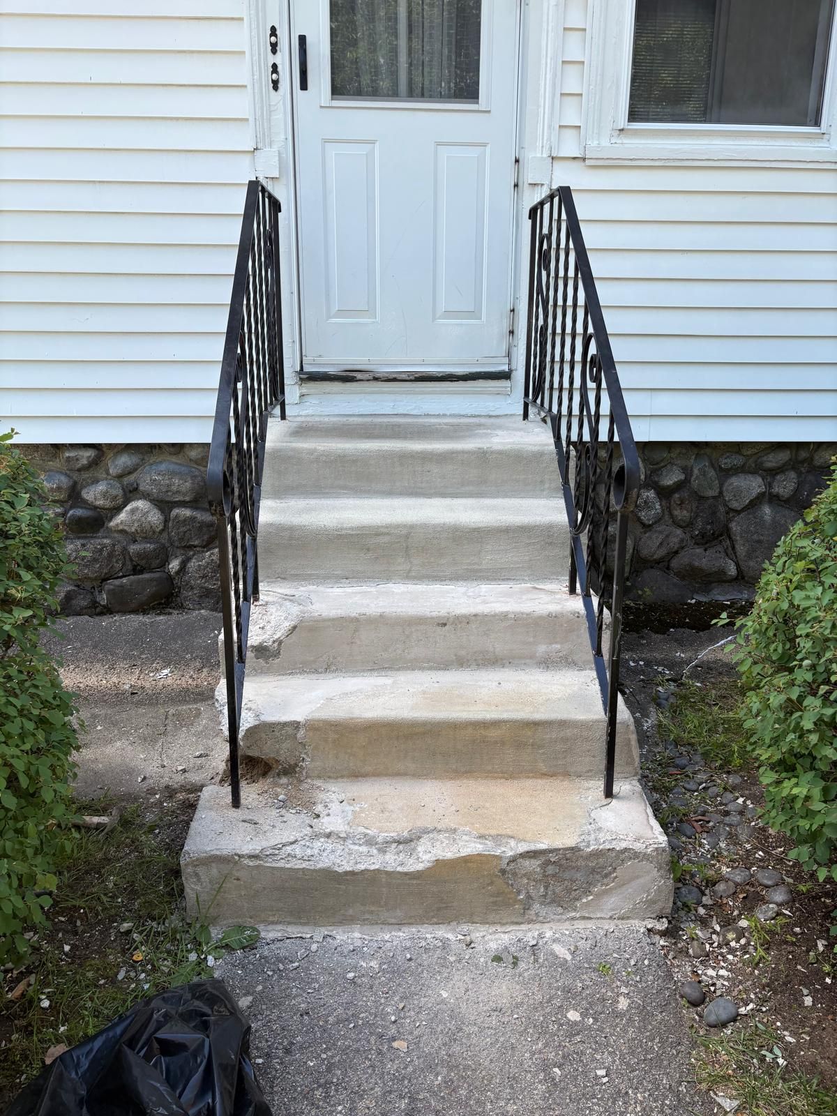 Concrete front steps with black railings leading to a white house door.