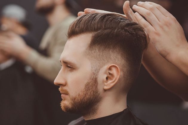 Barber styling a man’s short fade haircut in a busy barbershop