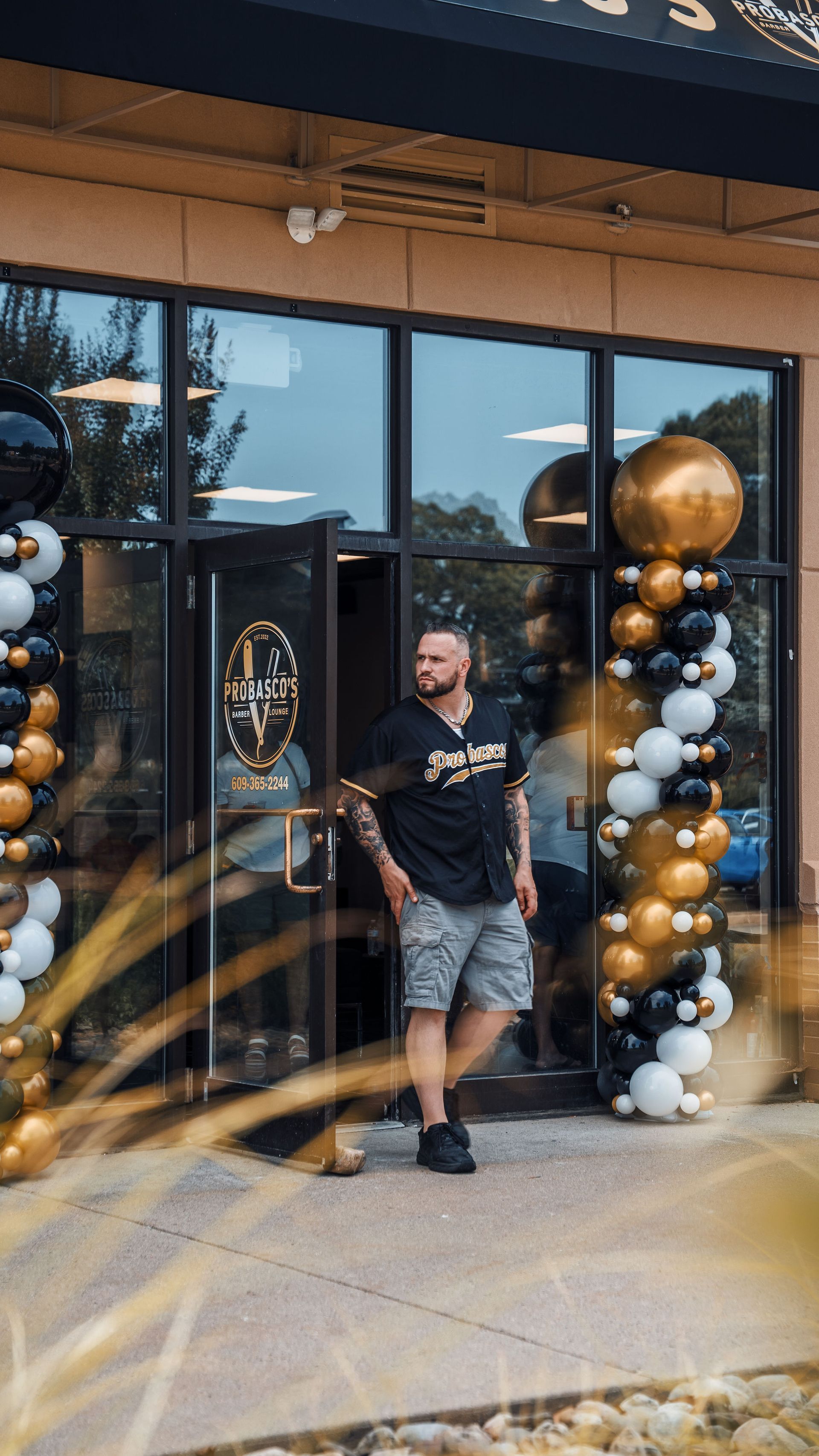 Man standing at a storefront entrance decorated with black, gold, and white balloons.