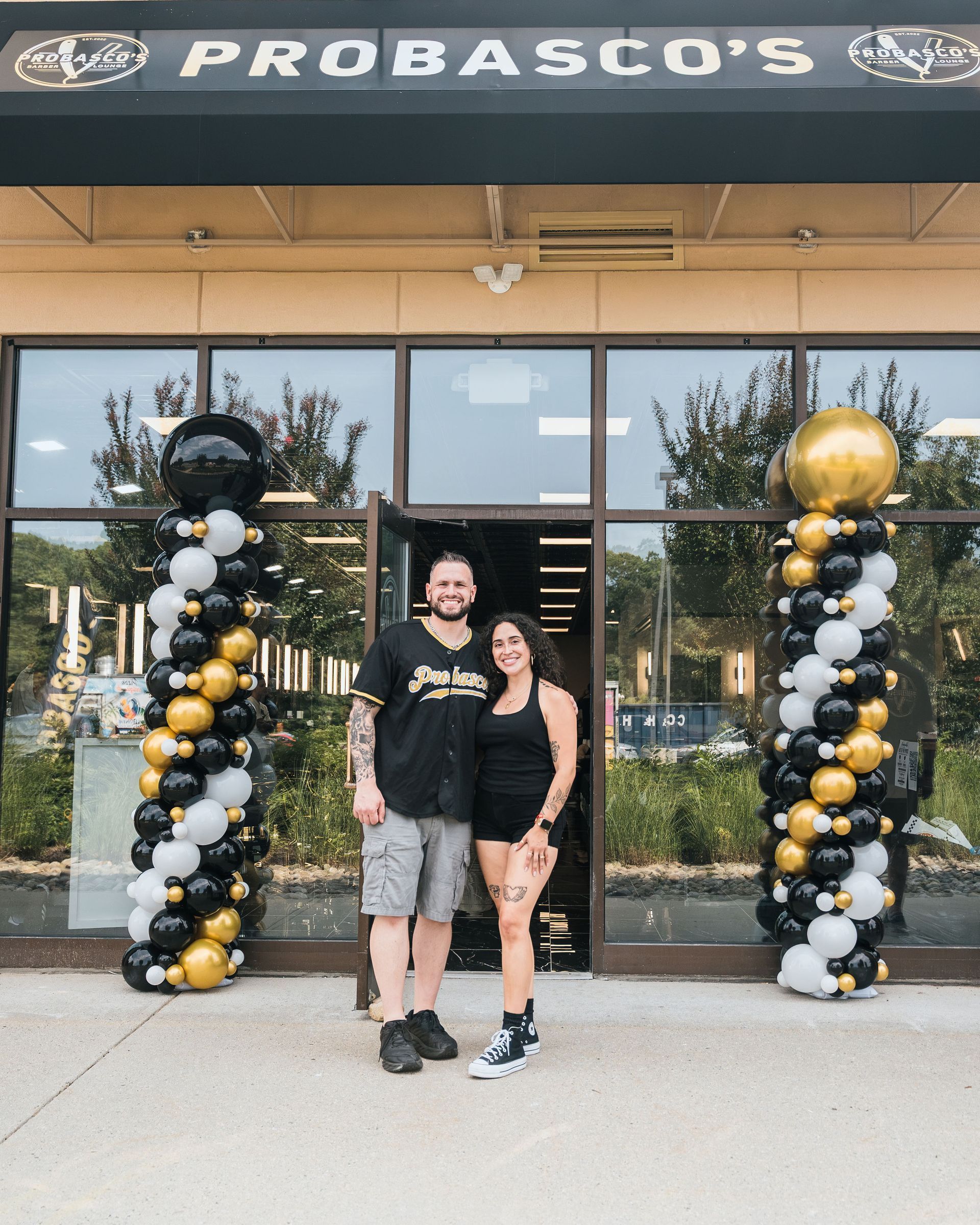 Two people posing outside Probasco’s under black, white, and gold balloon arches