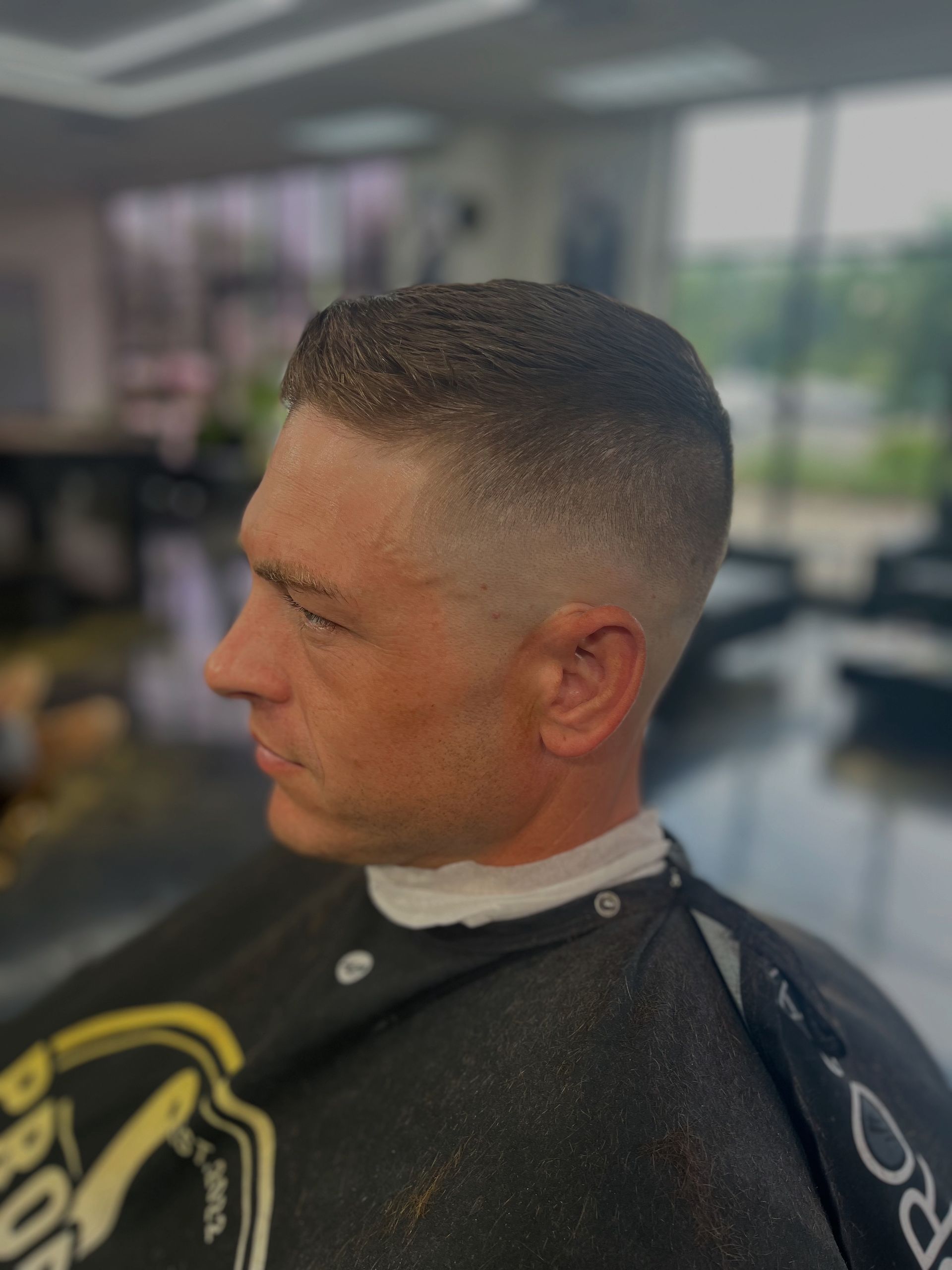 Man in a black cape with a fresh fade haircut sitting in a barber chair, side profile indoors
