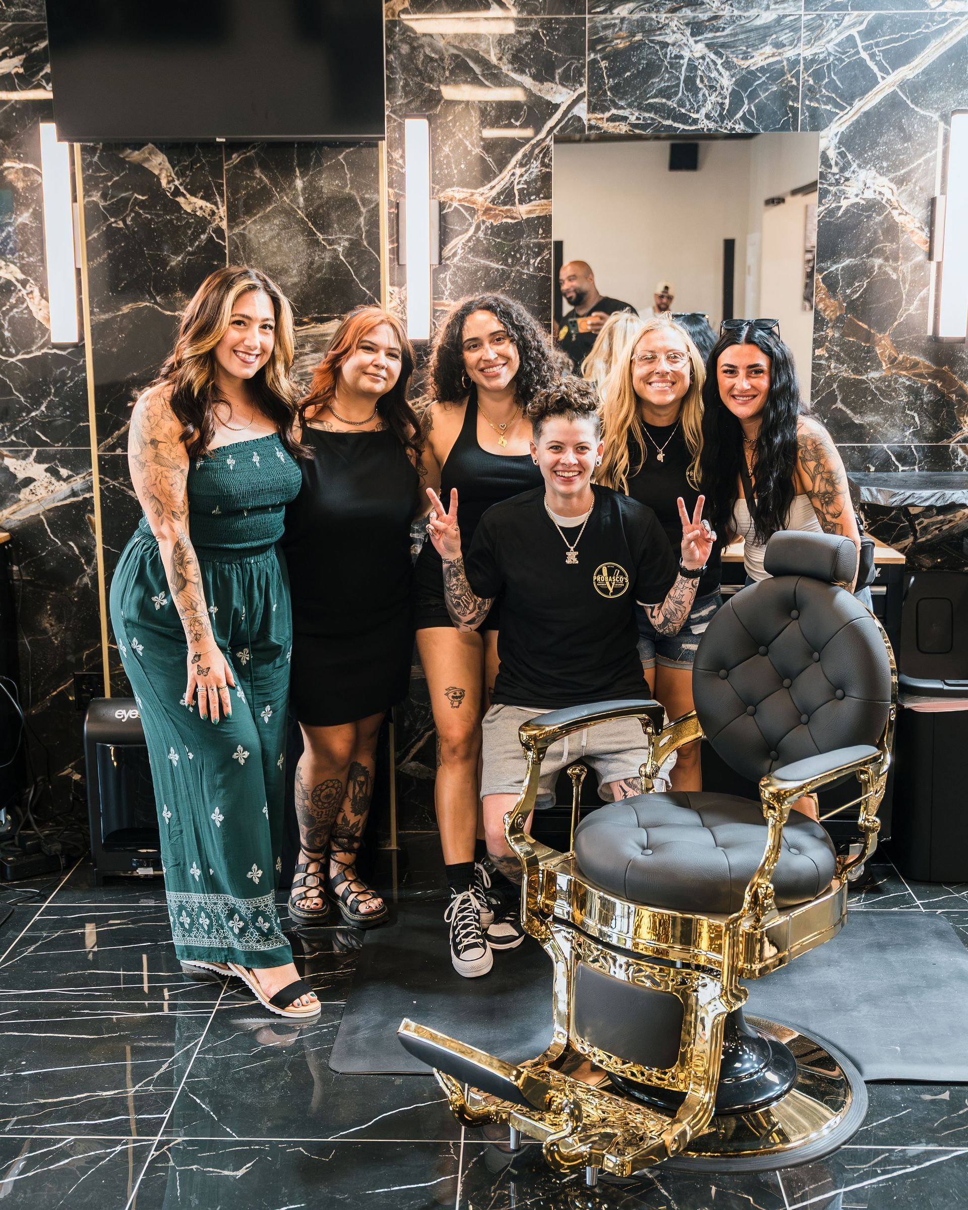 Six people posing together in a marble lobby beside a black-and-gold salon chair