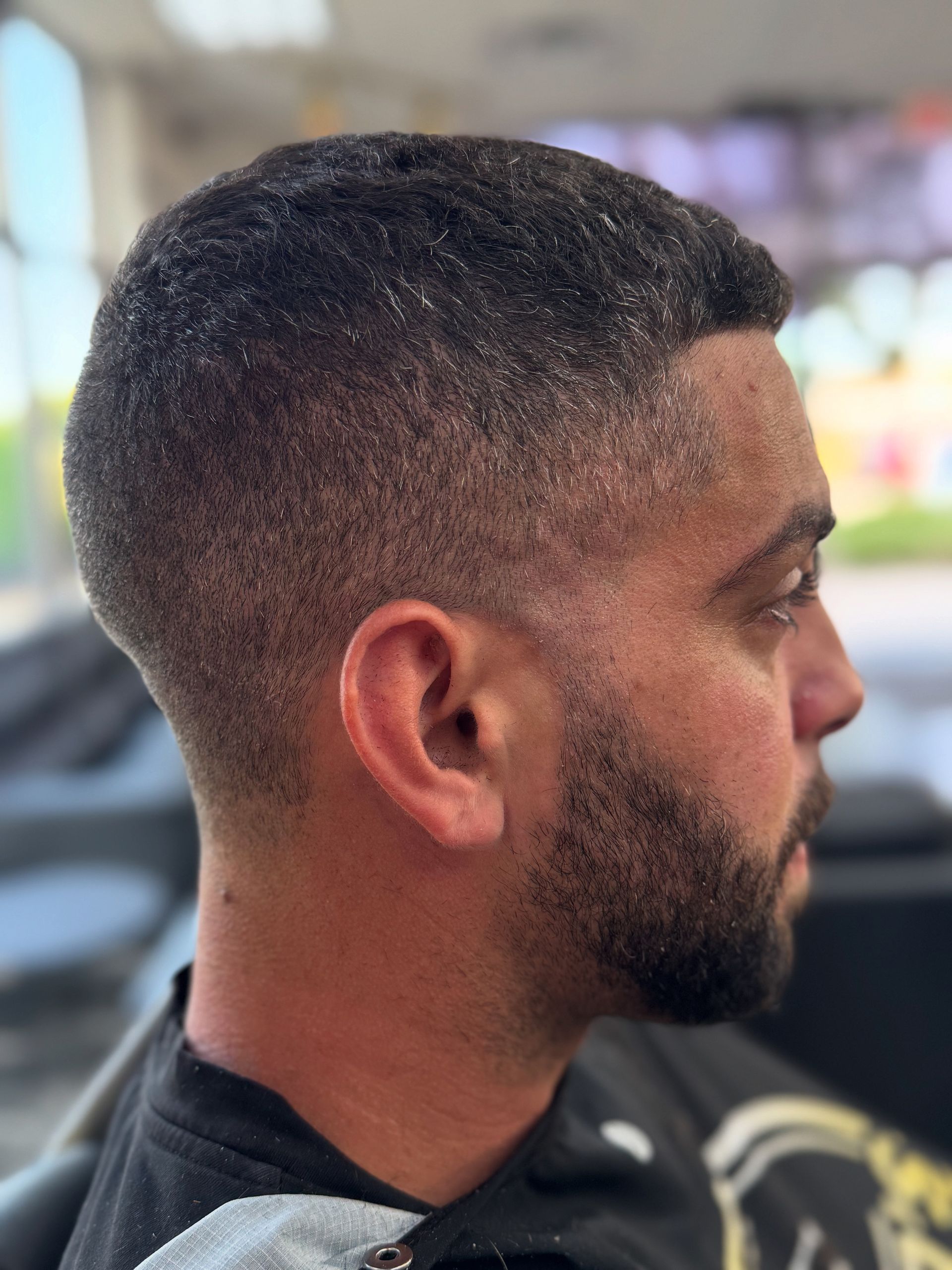 Side profile of a man with a short fade haircut and trimmed beard, seated outdoors in a black shirt.