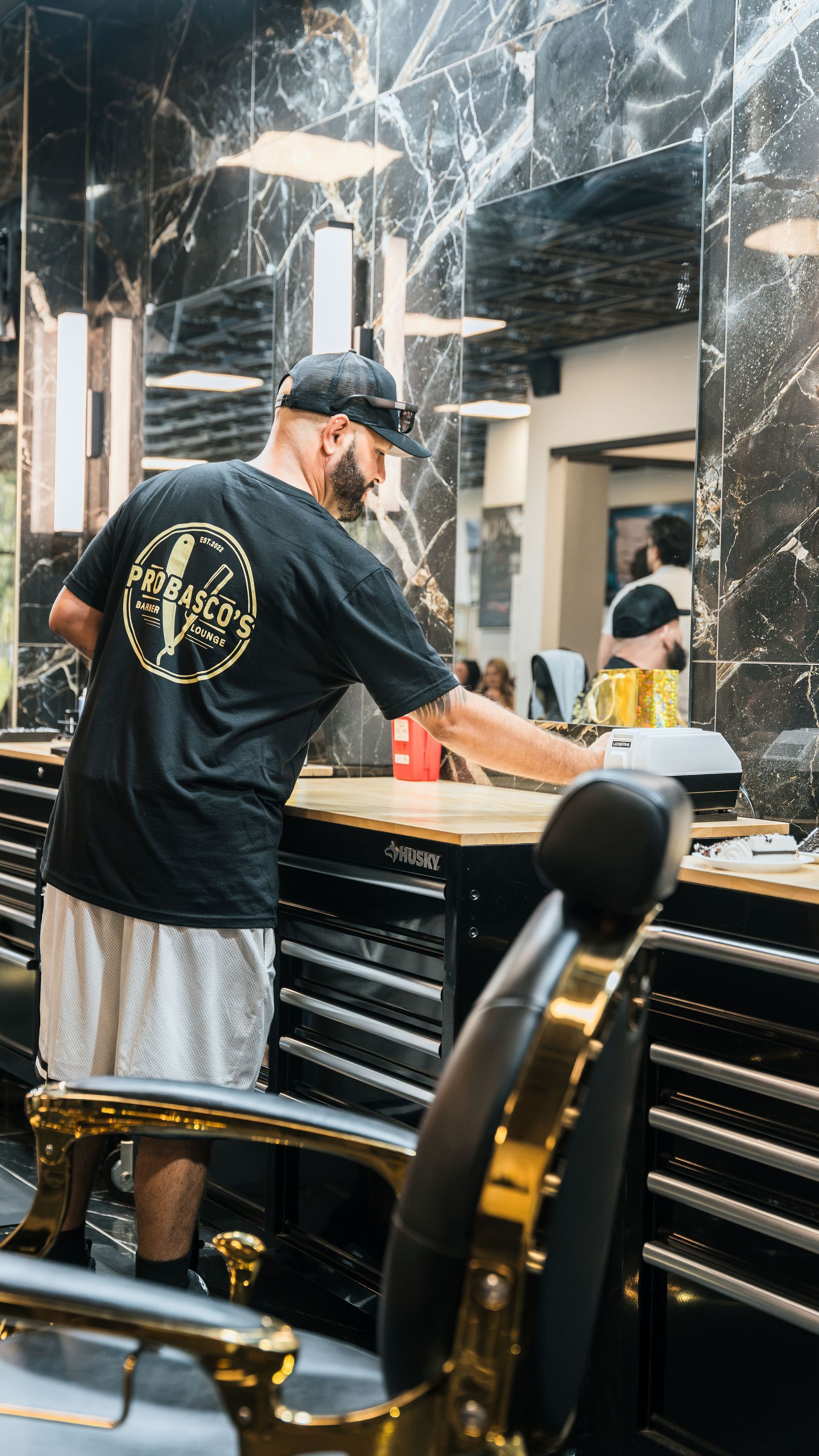 Man in black T-shirt works at a salon counter with mirrored walls and silver decor