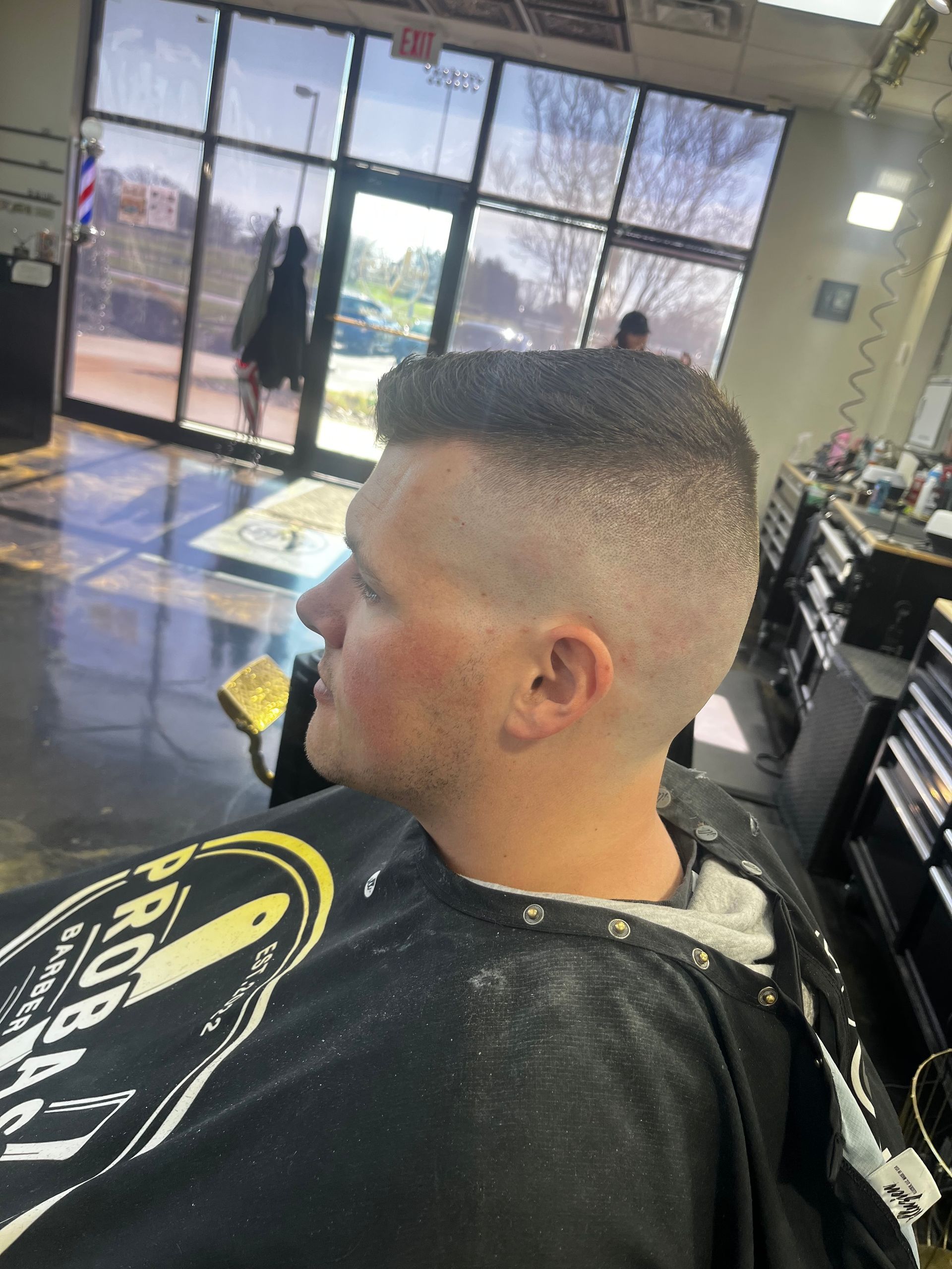 Person getting a fresh fade haircut in a barbershop, seated by a window.