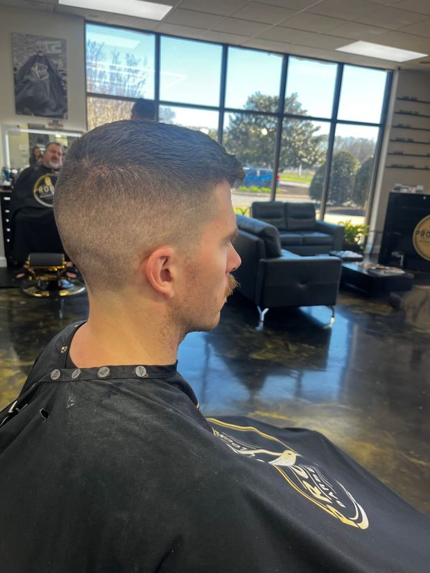 Side profile of a short fade haircut in a barber shop, with large windows and salon chairs in the background.