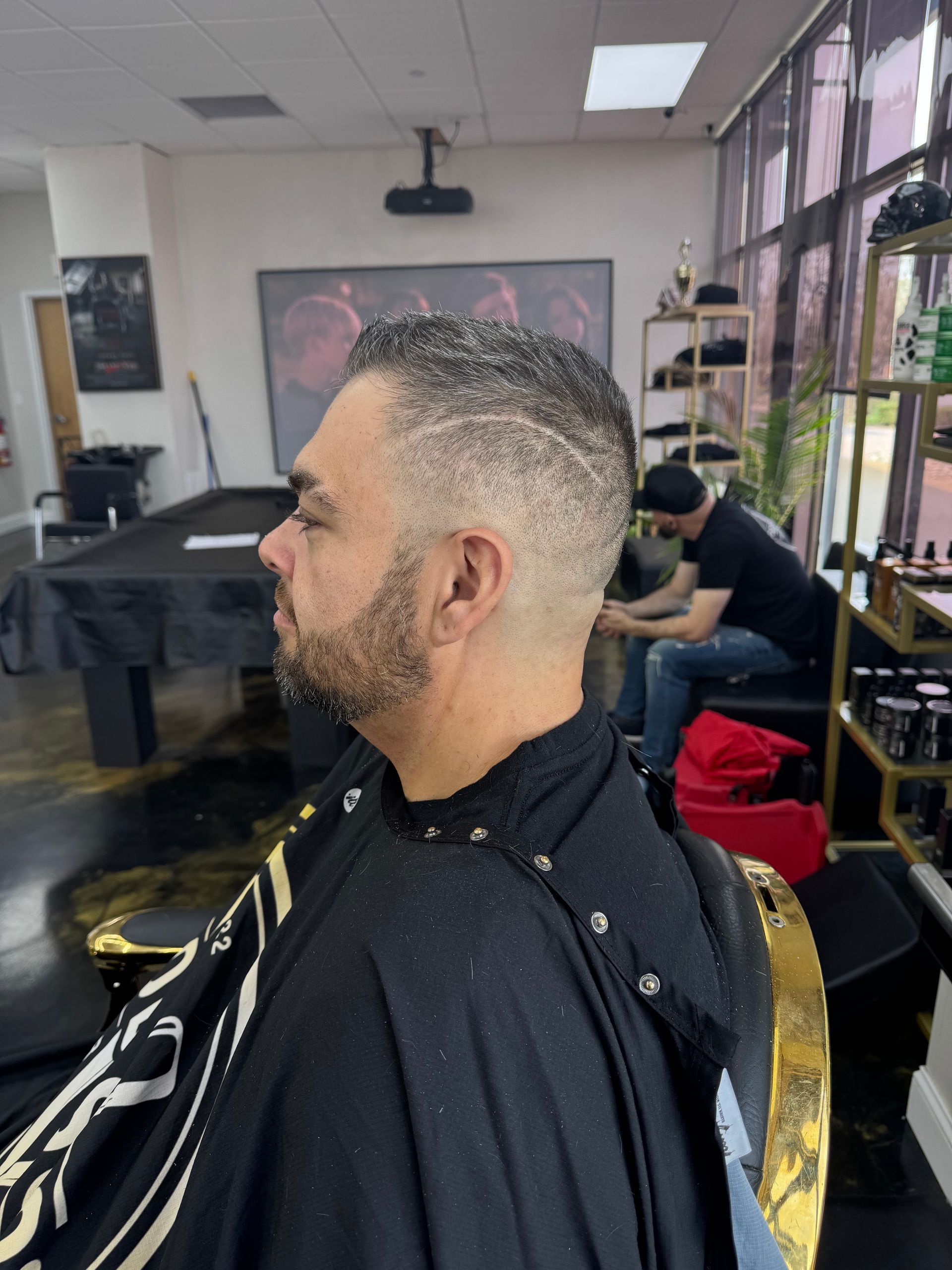 Man getting a fade haircut in a barbershop, seated in profile with barber tools nearby