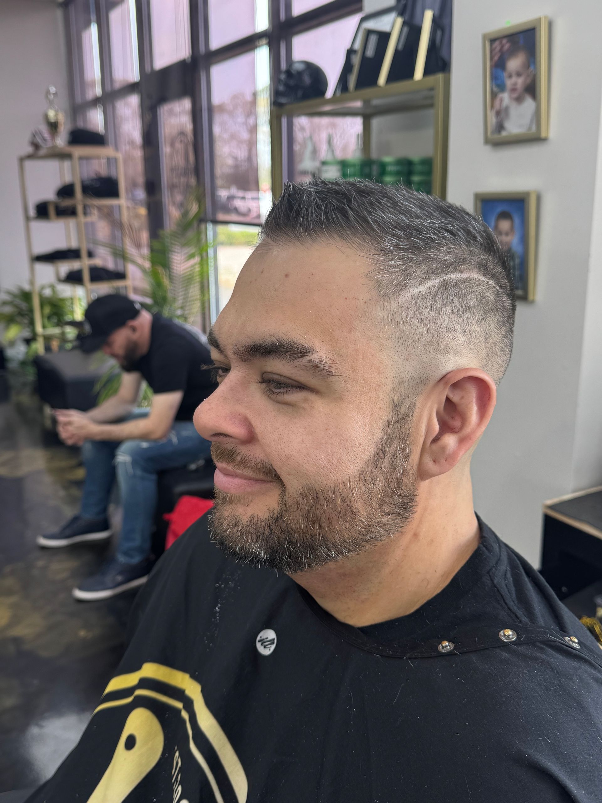 Man sitting in a barber chair with a fresh fade haircut, another person blurred in the background.