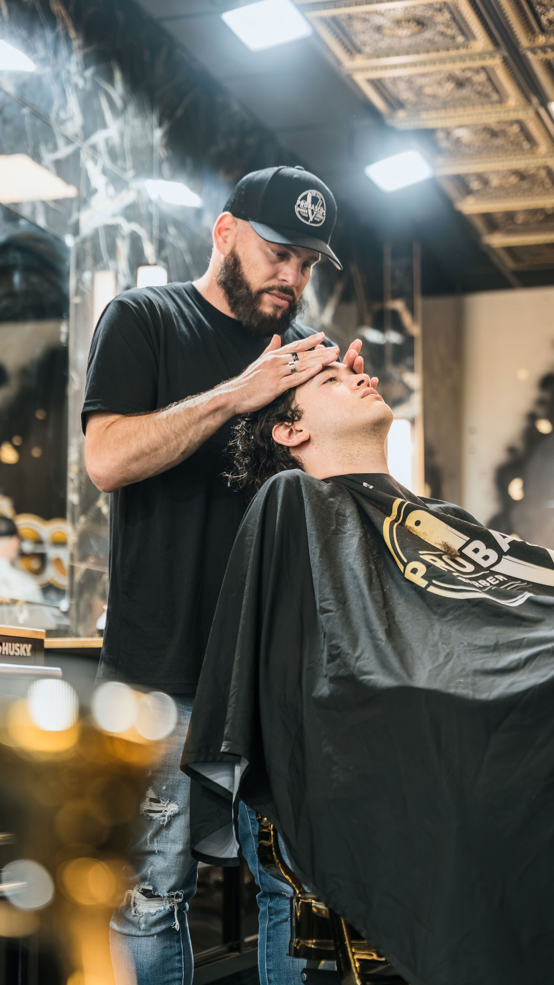 Barber trimming a client’s hair in a tattoo shop, with black cape and warm overhead lights.
