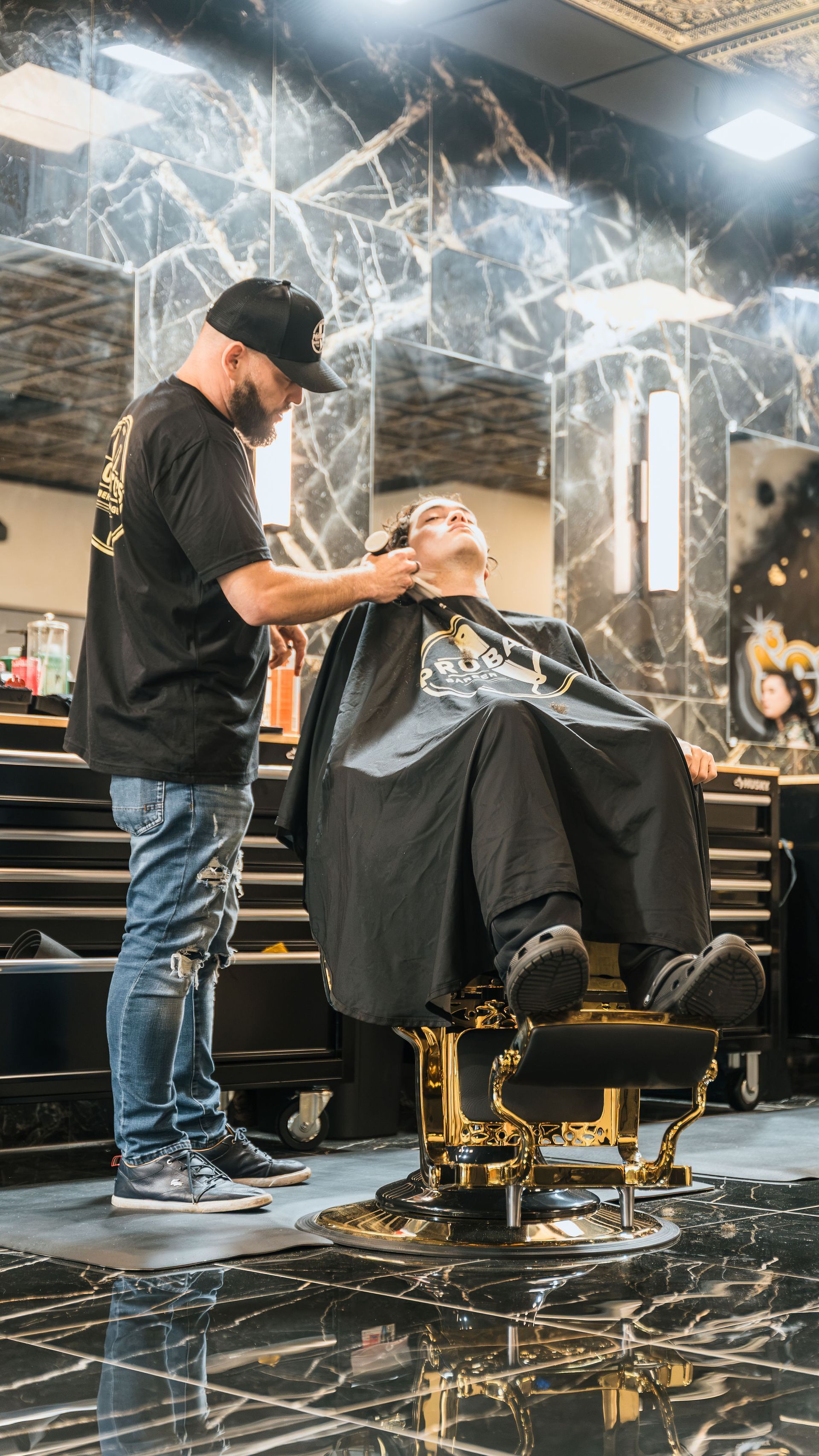 Barber cutting a client’s hair in a modern salon with marble walls and gold chairs