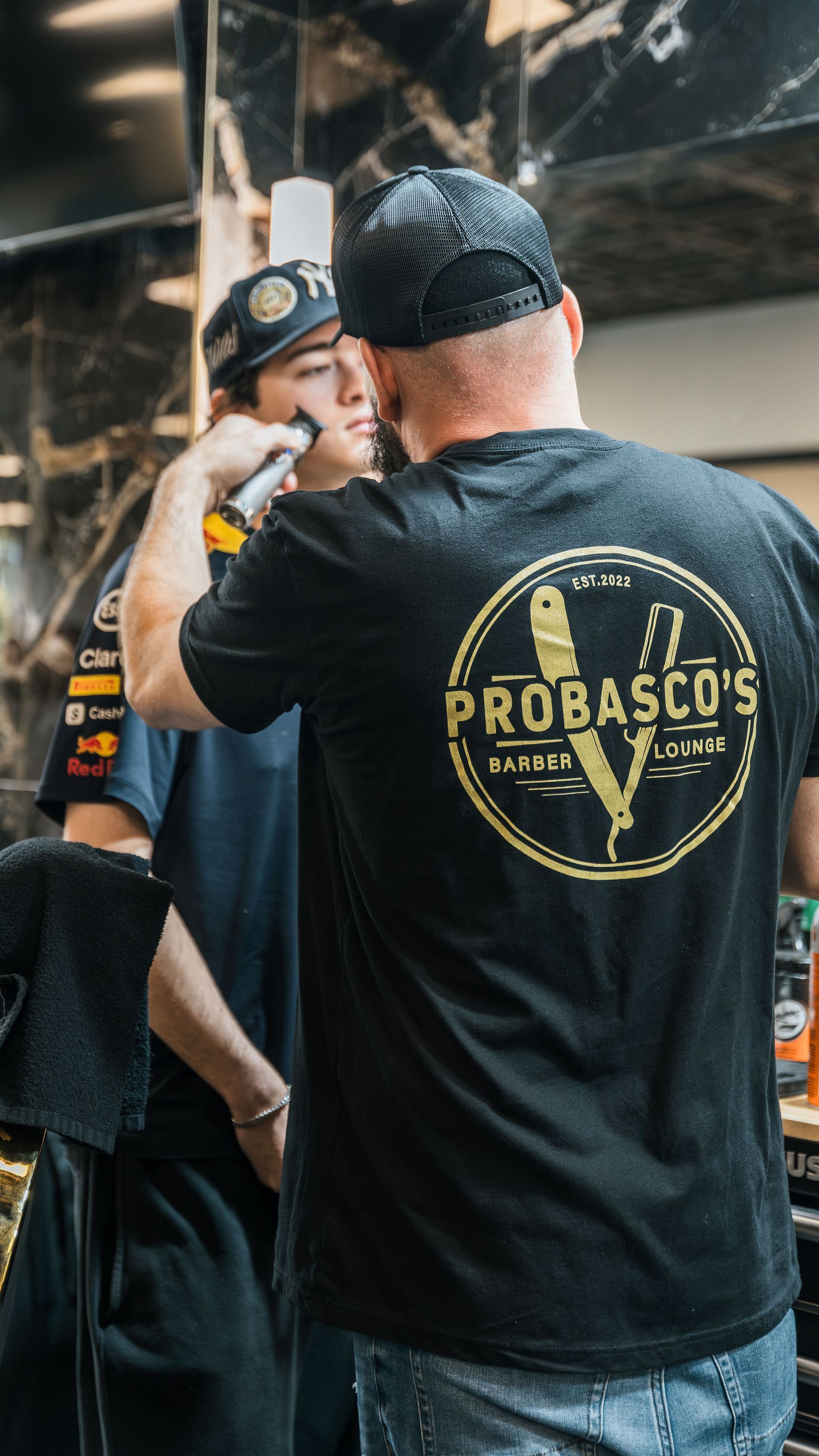 Two people in black shirts at a venue, one with a “PROBASCOS” logo on the back, smiling in conversation