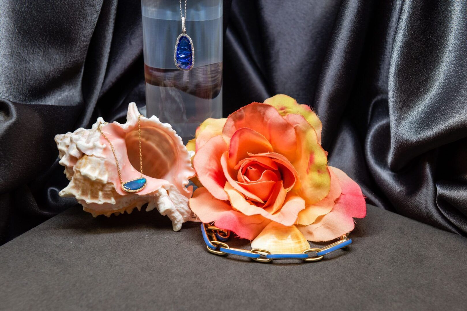 Jewelry display with a seashell, necklace, bracelet, flower, and backdrop.