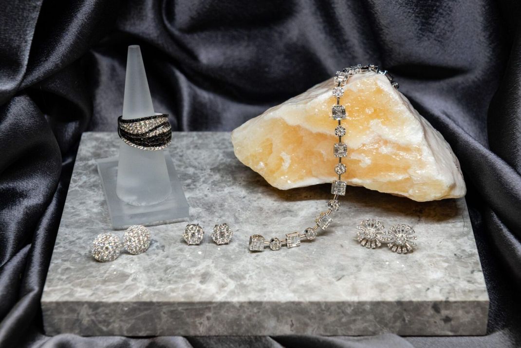 Jewelry display: black and silver ring on a stand, bracelet on a rock, earrings, set on a gray surface with dark gray fabric.