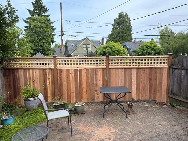 A backyard patio area featuring a new cedar privacy fence with lattice trim, a small metal table, and a chair.