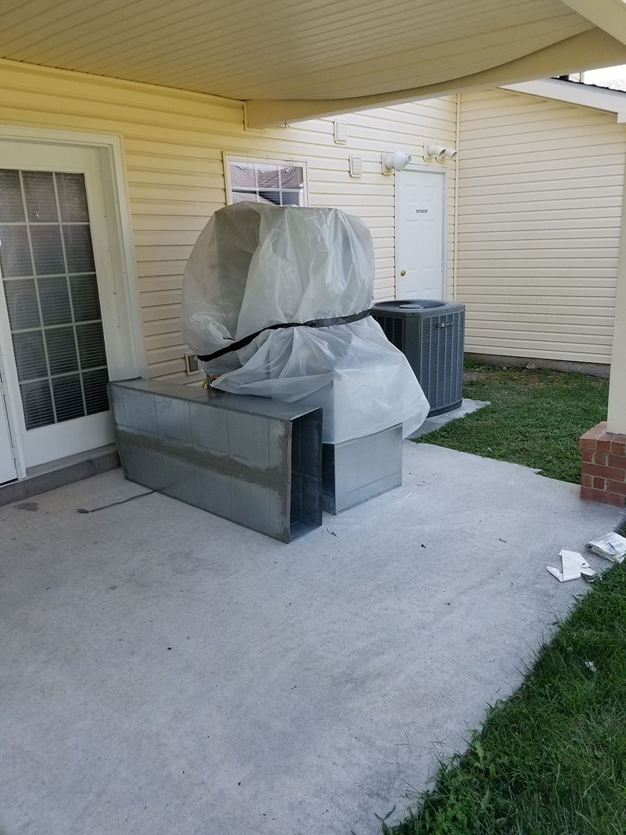 A bunch of air conditioners are sitting on a concrete patio in front of a house.