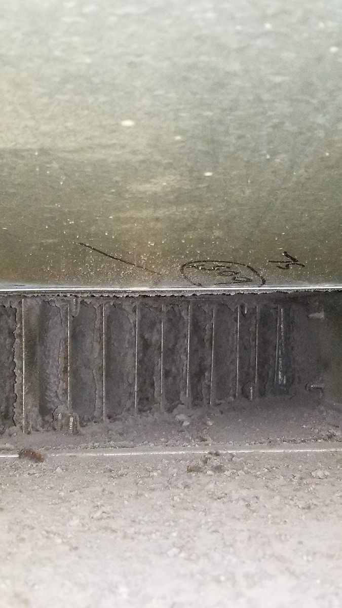 A close up of a dirty air vent on a concrete floor.