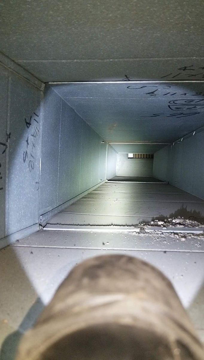 A person is looking down a duct with a flashlight.