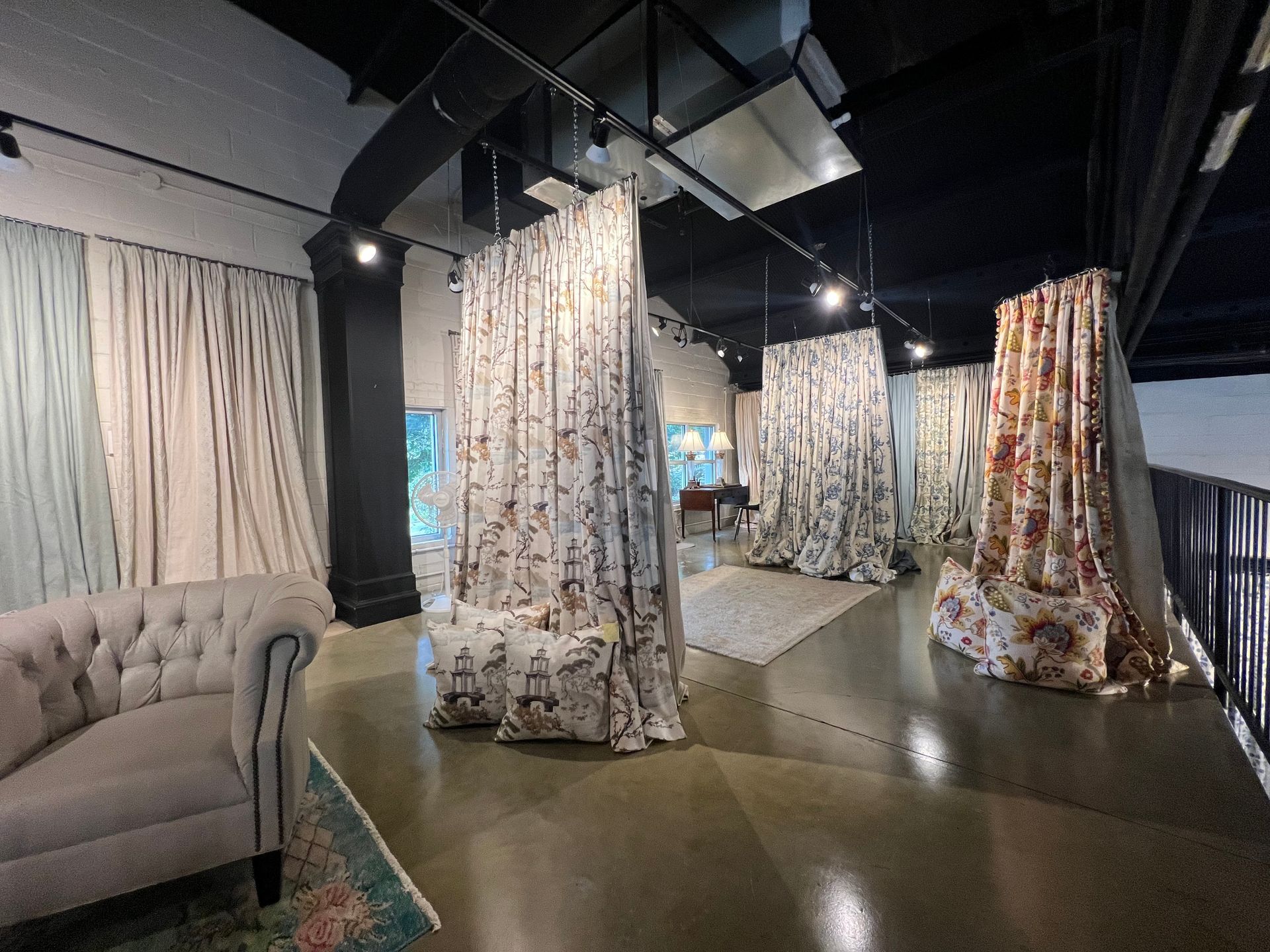 A fabric showroom featuring several displays of hanging patterned curtains and matching throw pillows on concrete floors.