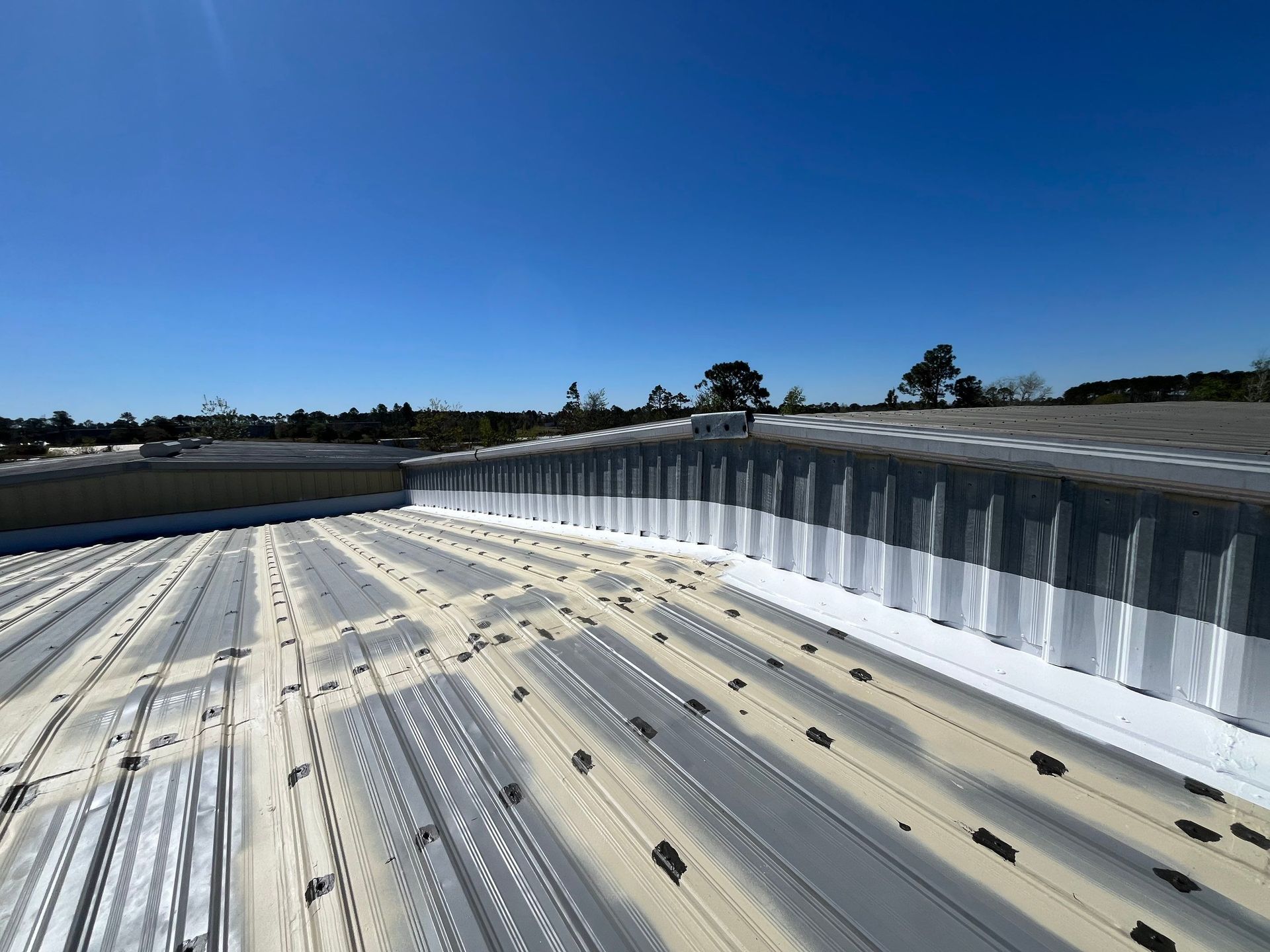 Metal roof with white sealant, against a clear blue sky.