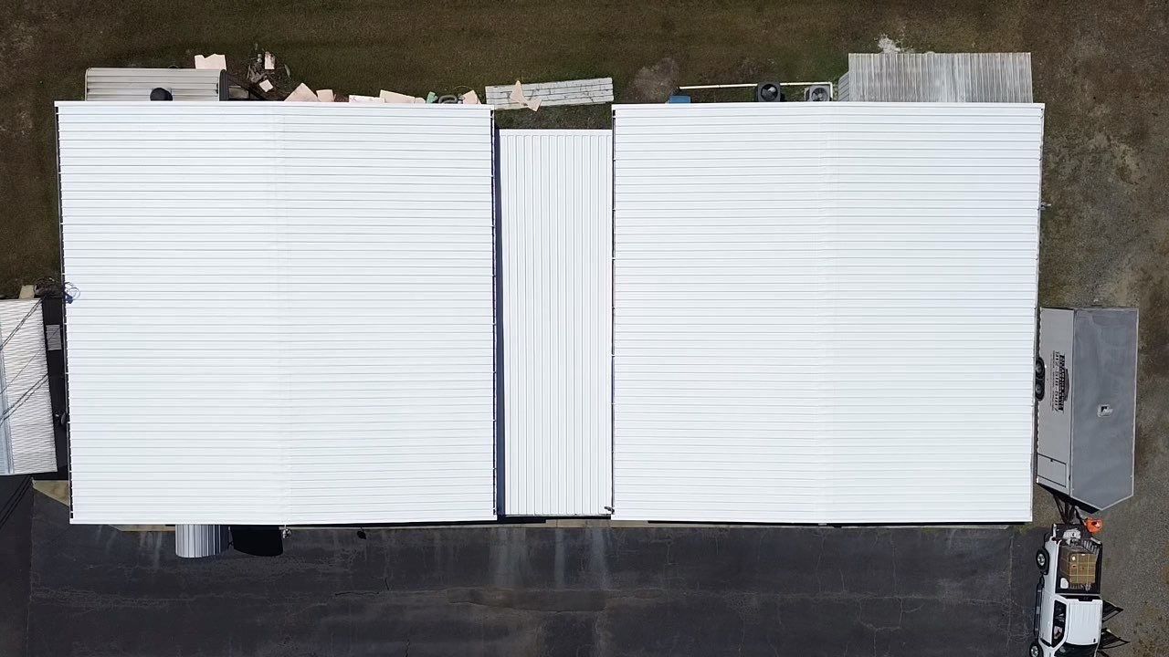 Aerial view of a white metal-roofed building with construction materials and a person on the roof.