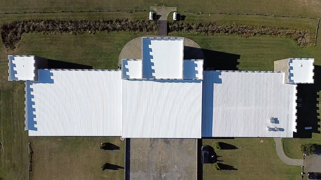 Overhead view of a white-roofed building resembling a castle with four corner turrets, set on green grass.