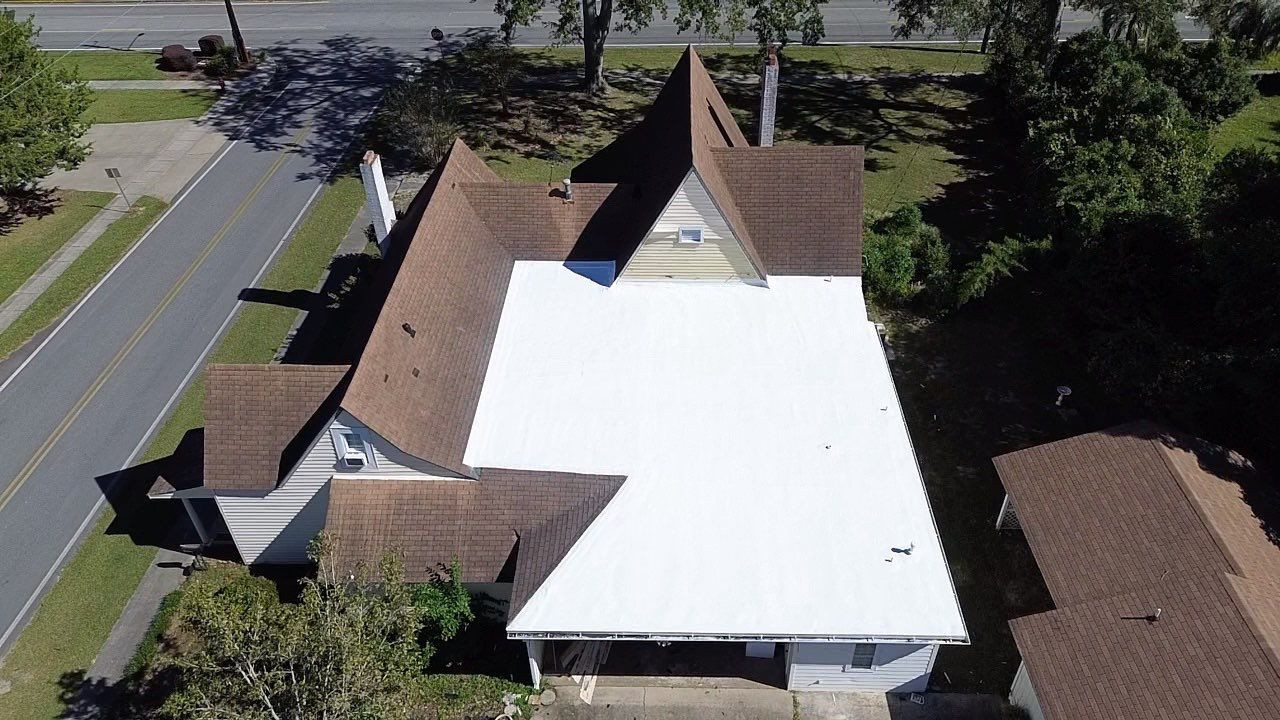Aerial view of a house with a white flat roof and brown shingle roof sections.
