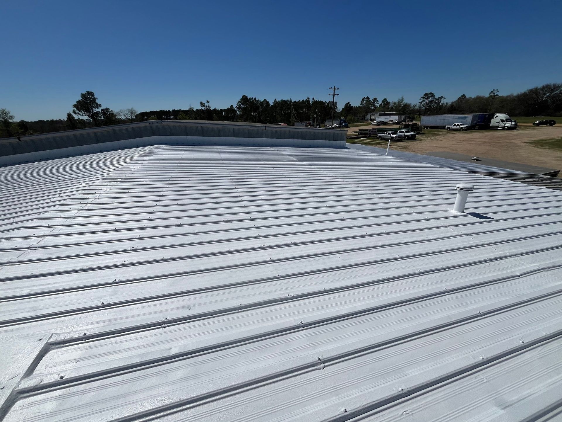 Metal roof with white coating, bright blue sky, and surrounding trees.