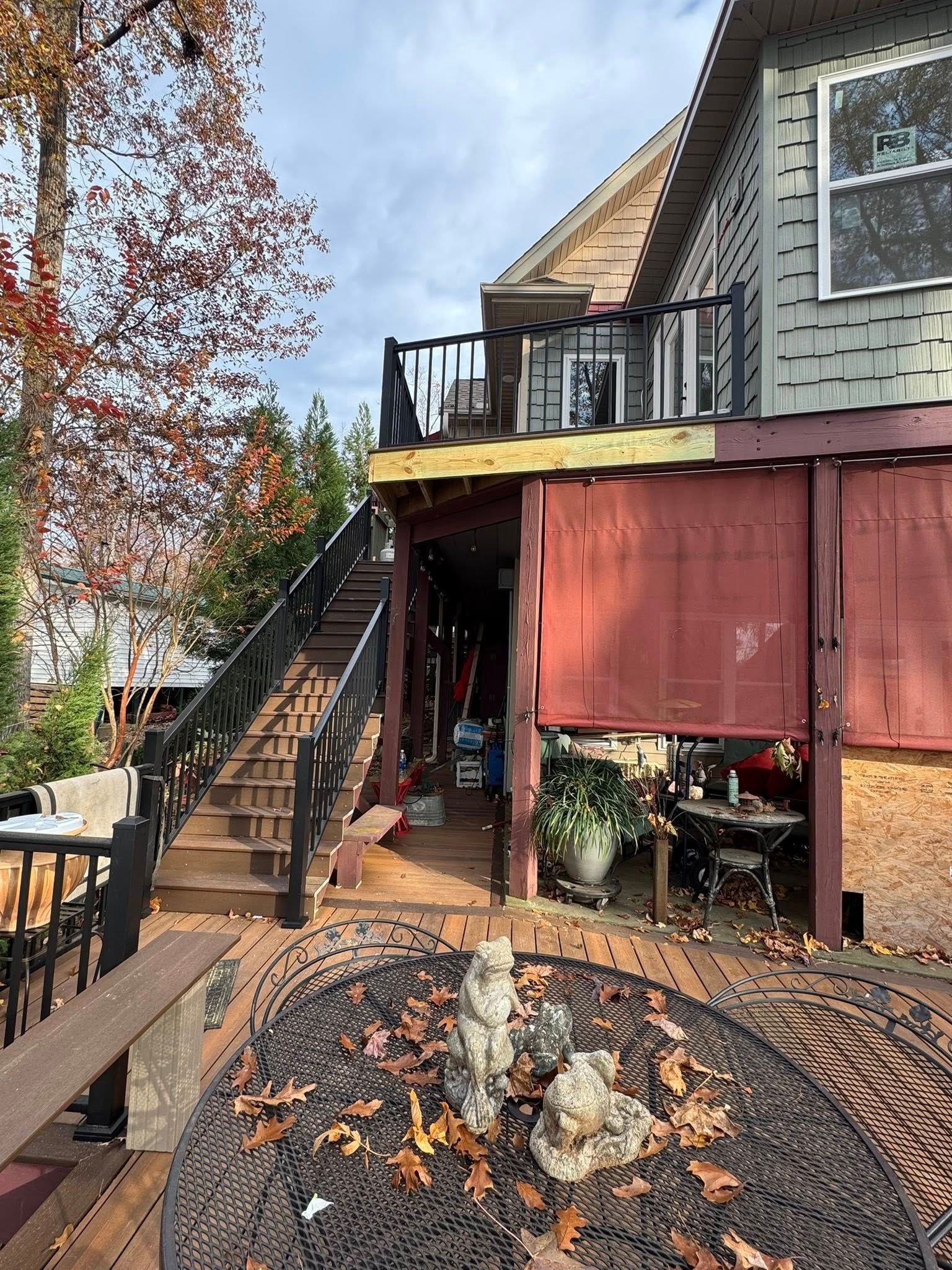Wooden deck with stairs, partially covered by red canvas, leading to a house. Autumn leaves and a fire pit in view.