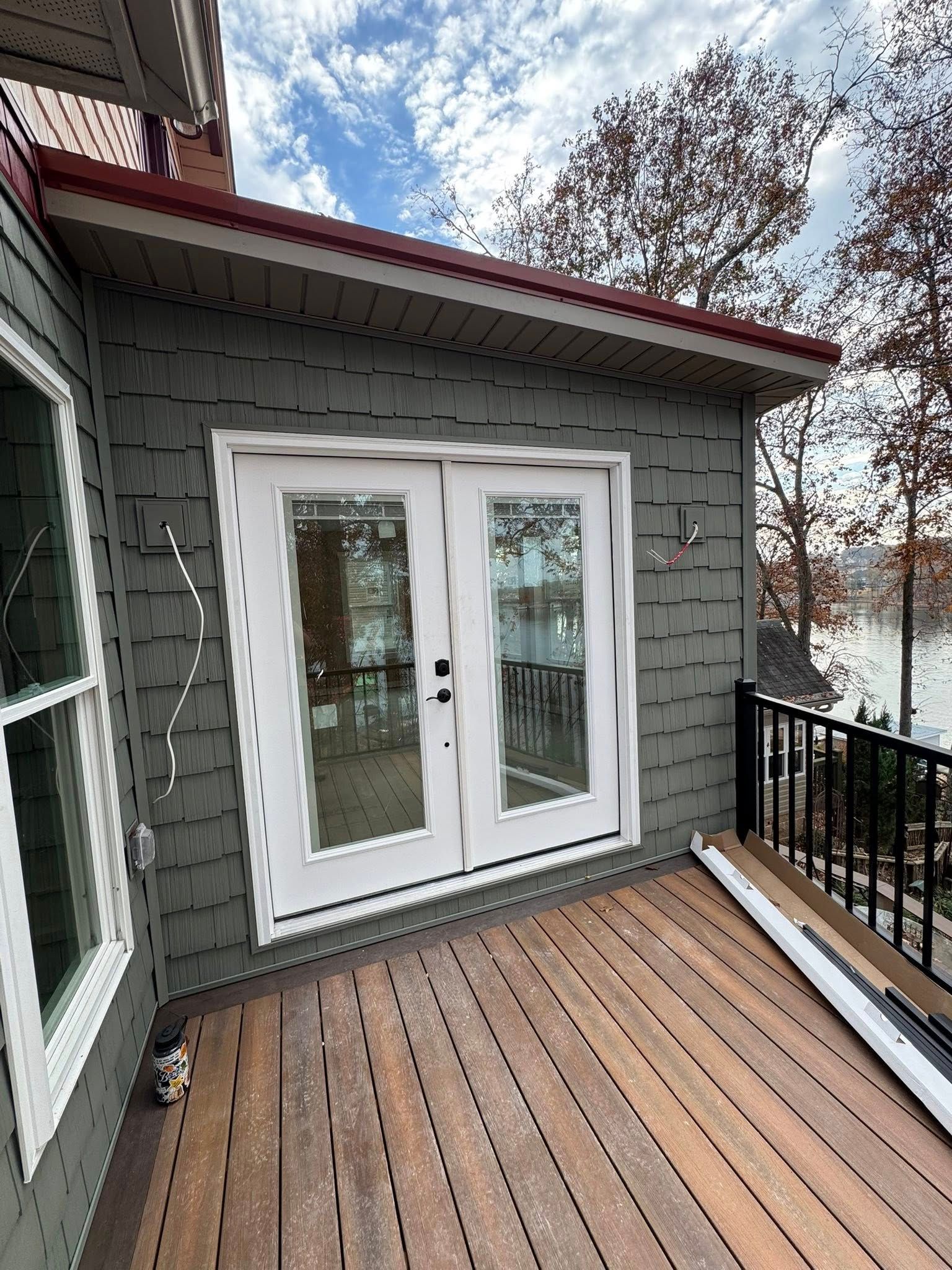 French doors leading to a wooden deck with black railing and lake view, green siding, blue sky.