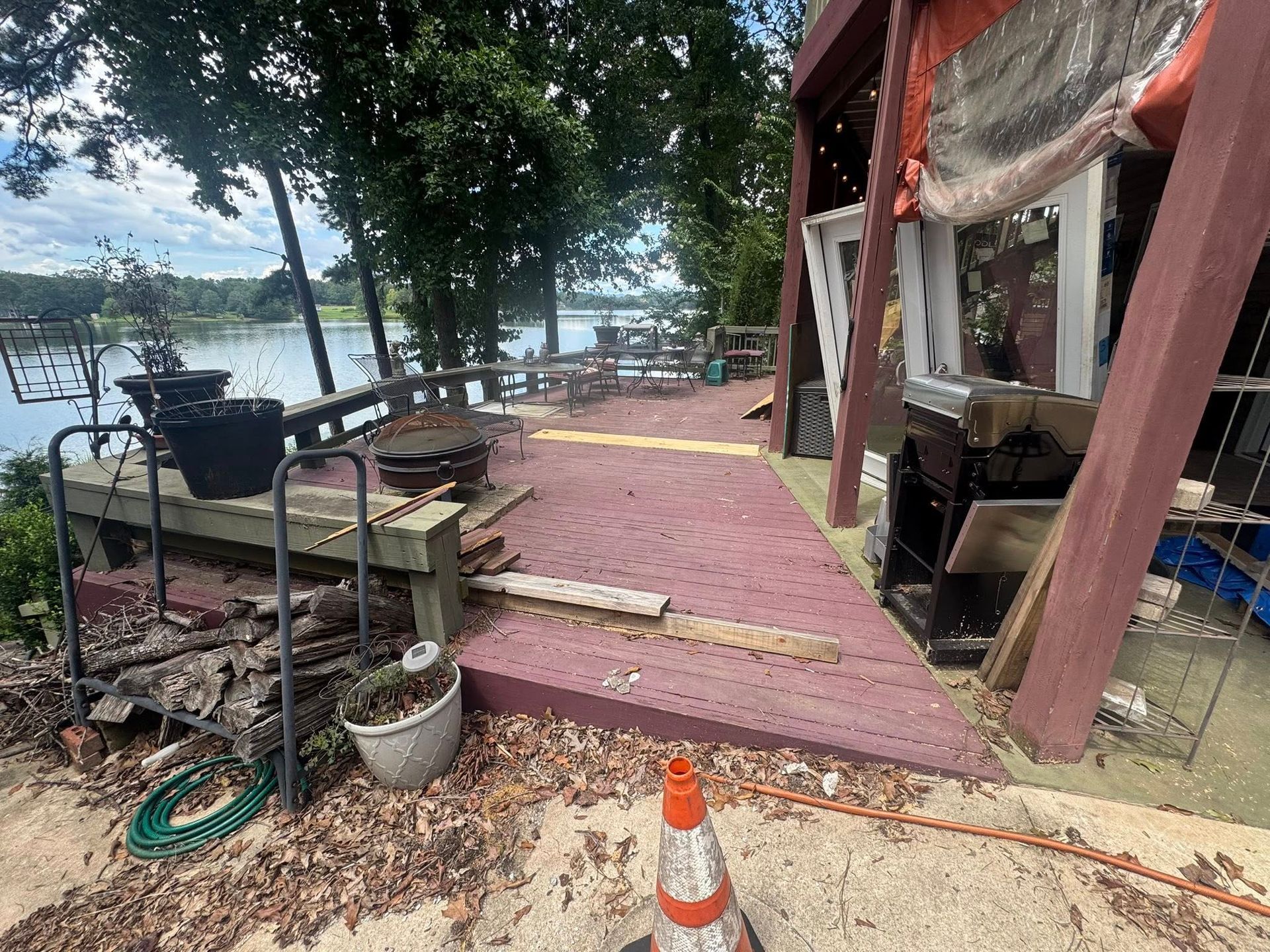 A deteriorating outdoor deck with debris, overlooking a lake. Reddish-brown wood, fallen leaves, and construction materials.