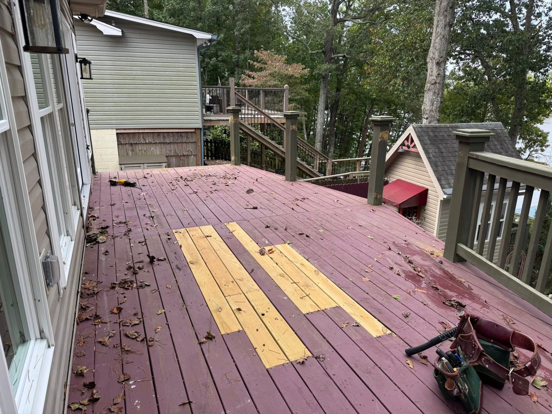 Deck with damaged planks, house in background, leaves scattered.