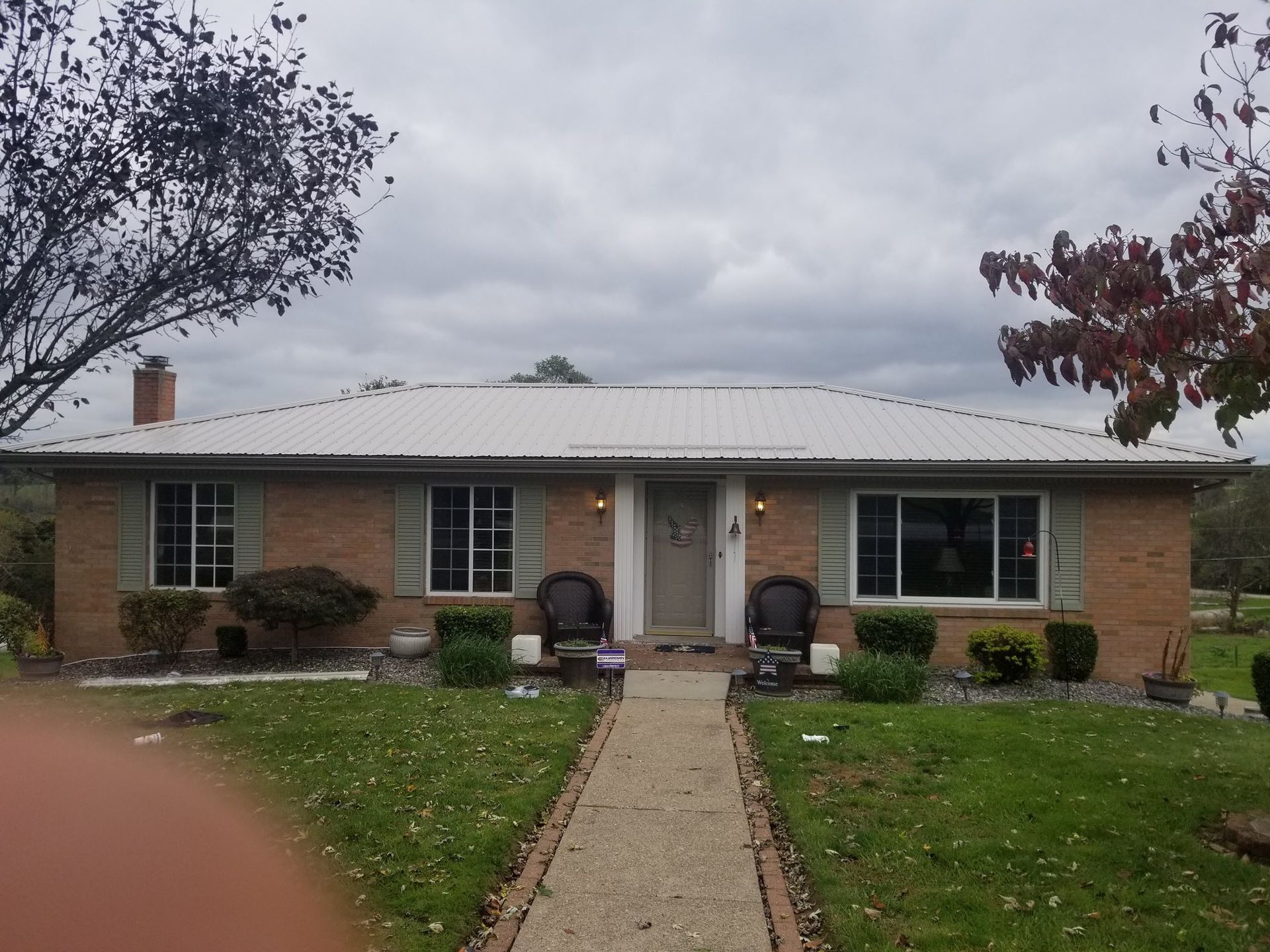 Brick ranch home with metal roof and walkway leading to the front door, cloudy day.