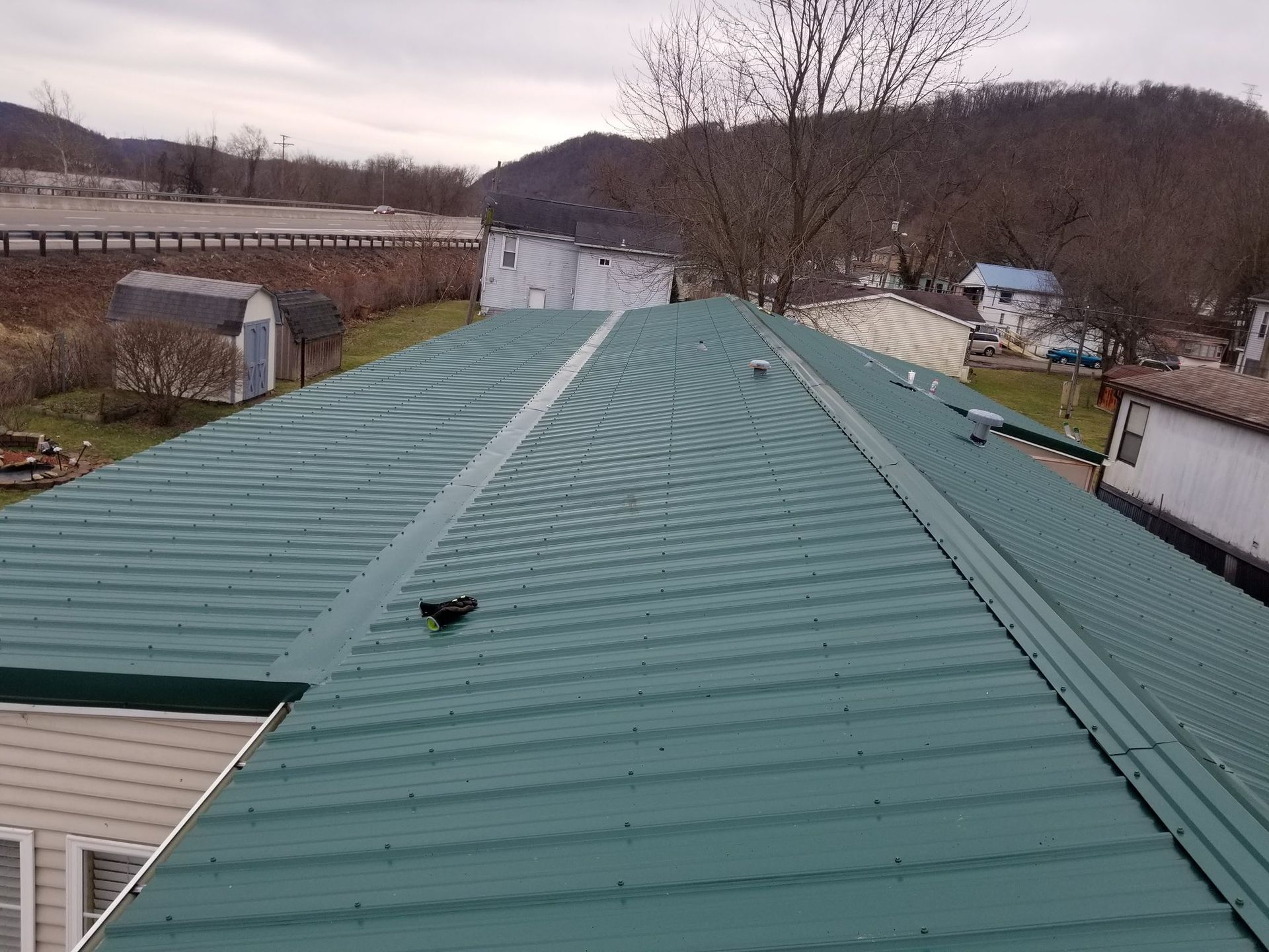 Green metal roof on a building, angled view, with a backdrop of a cloudy sky and landscape.