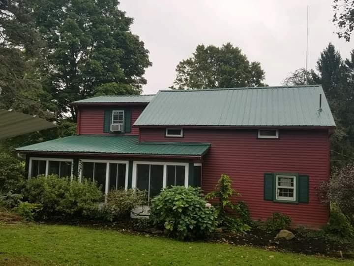 Red house with green metal roof and shutters, a screened porch, and surrounding trees.