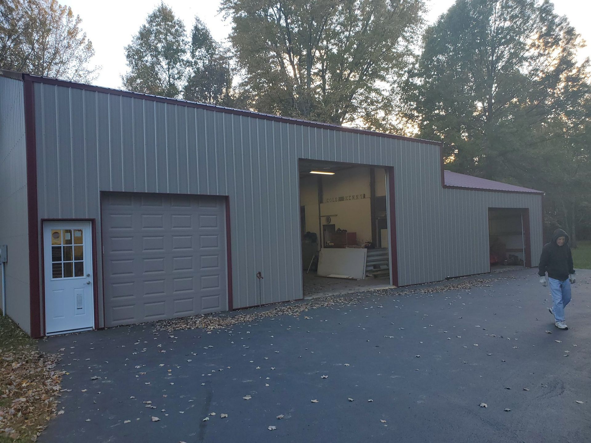 Gray metal building with three garage doors and a person walking on the driveway.