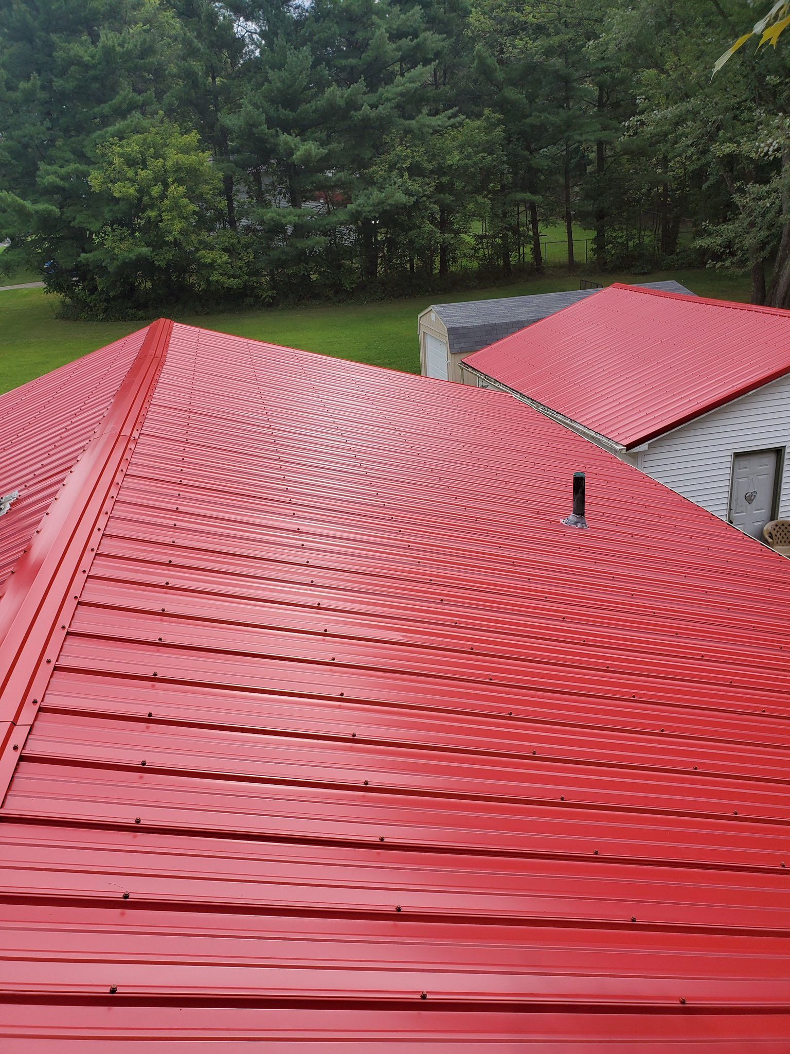 Red metal roof of a house with a pattern, in a green outdoor setting.