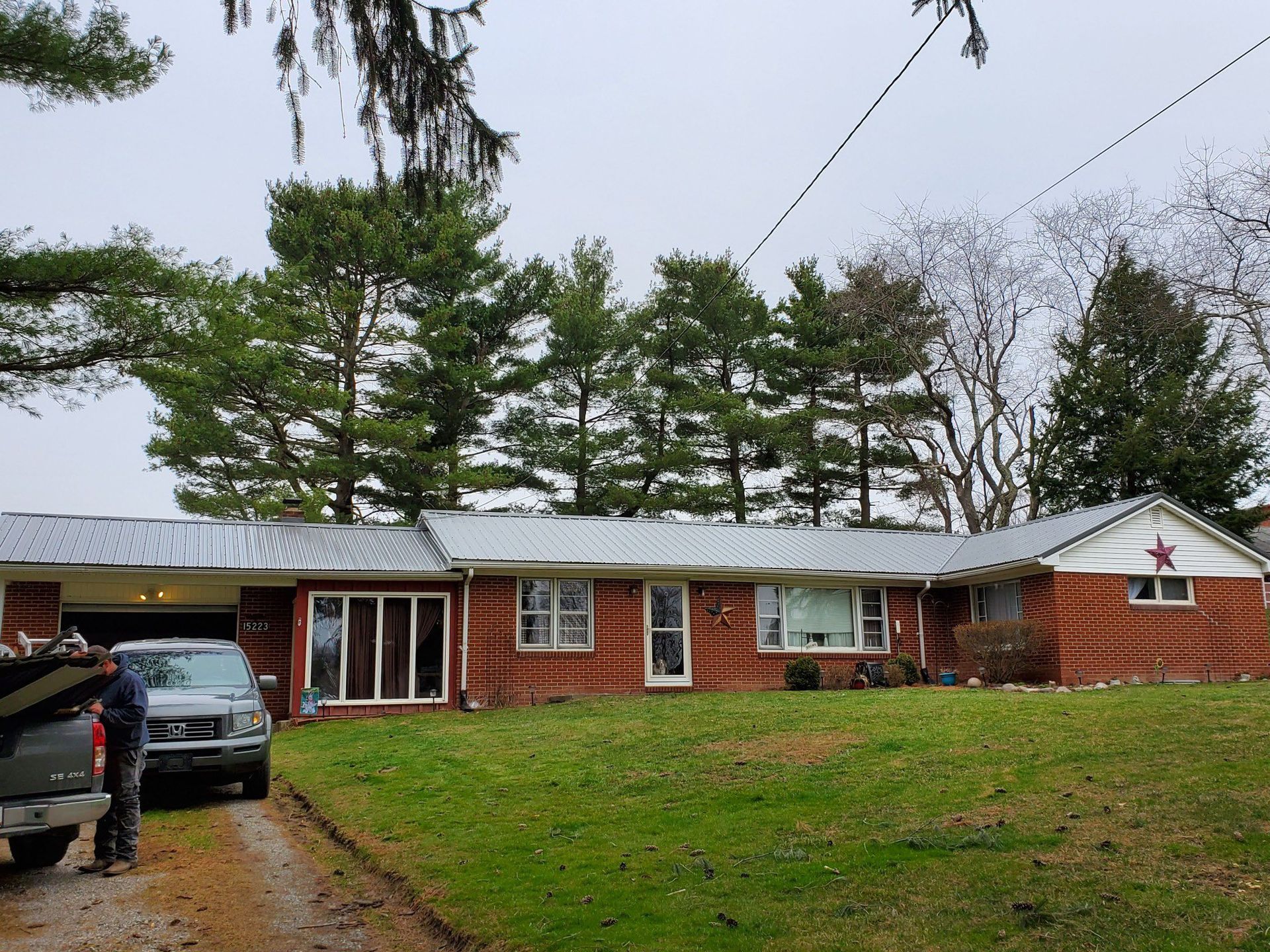 Red brick ranch house with a metal roof; a green lawn, and a driveway with a truck are in the foreground.