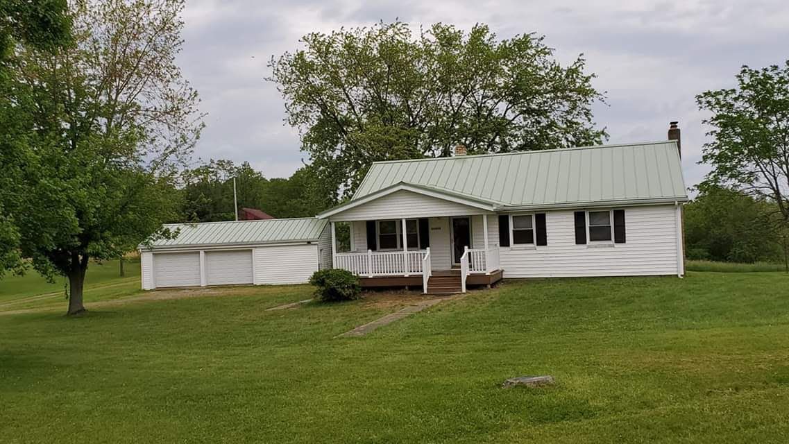 White house with green roof and attached garage on a grassy lot, cloudy sky.