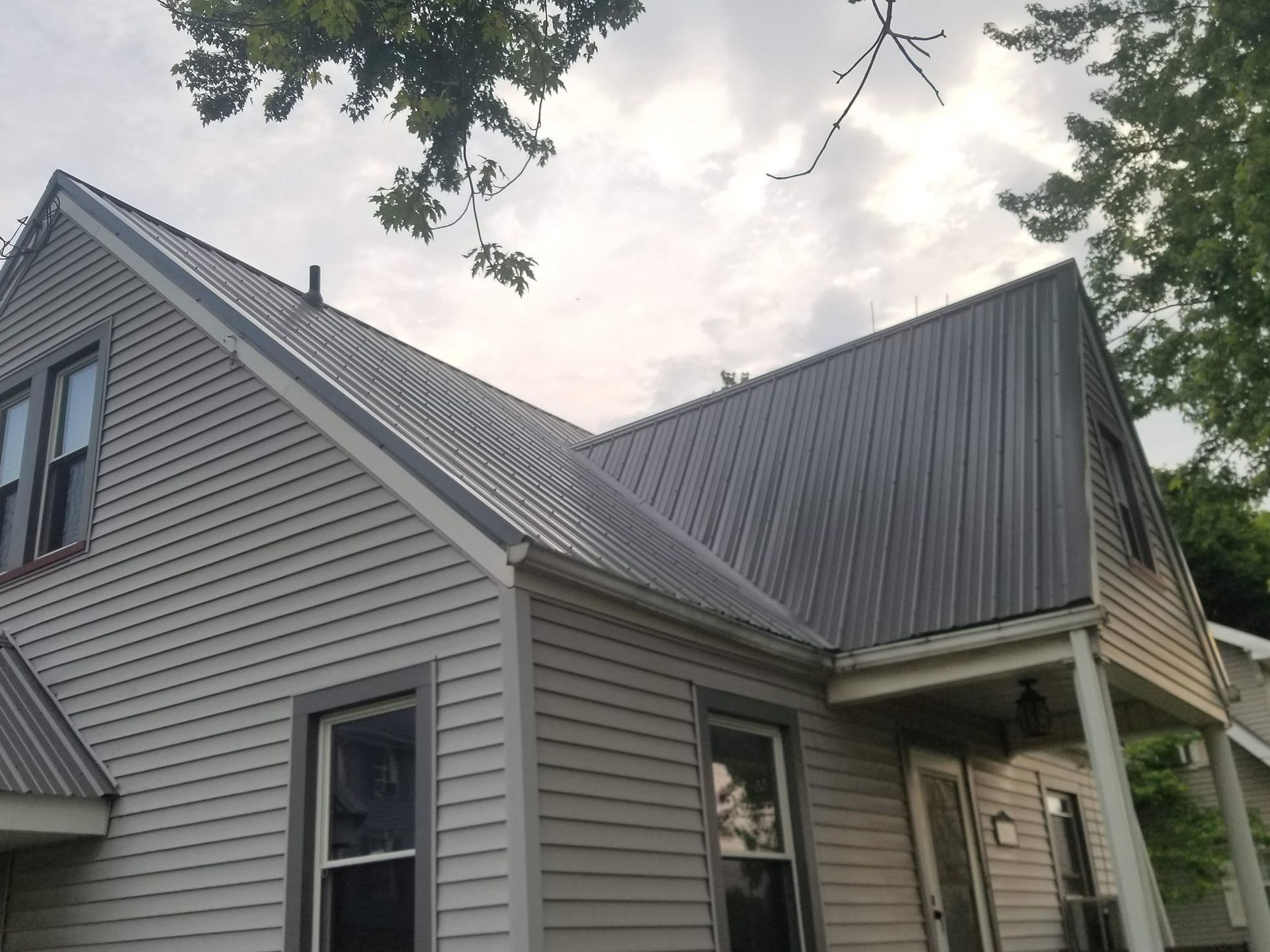 House with gray metal roof and siding, windows, and a porch under cloudy sky.