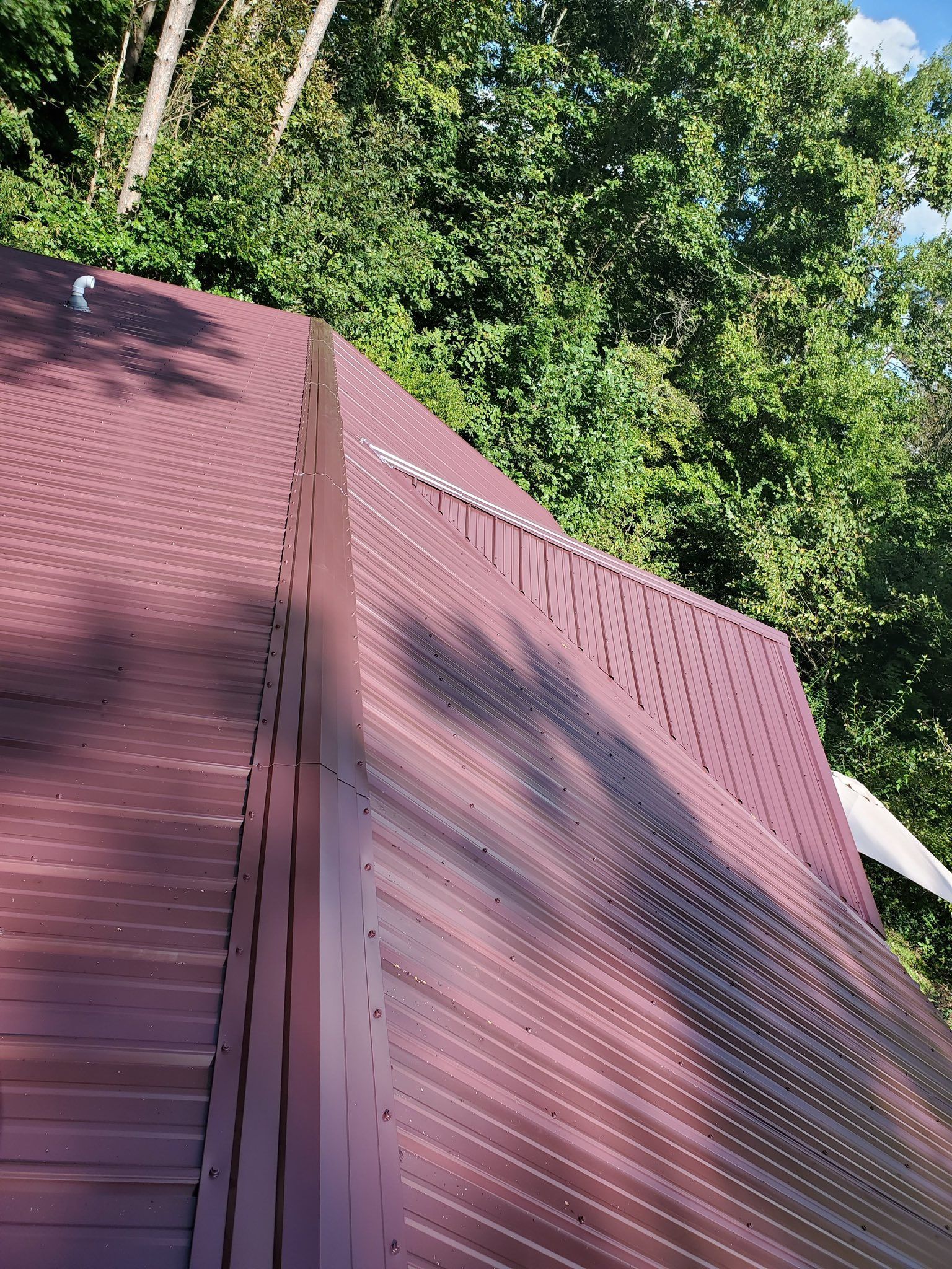 A brown metal roof with a perforated pattern, surrounded by green trees.
