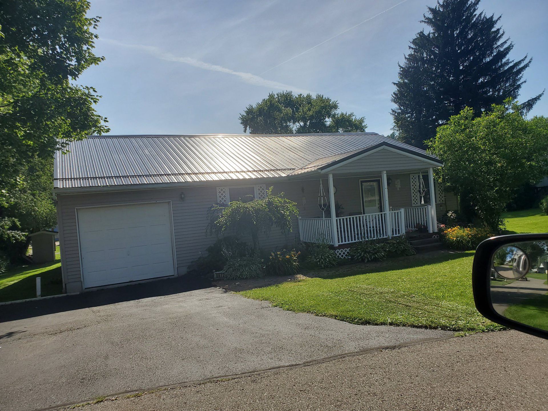 A gray house with a metal roof and attached garage, small porch with white railing, and driveway.
