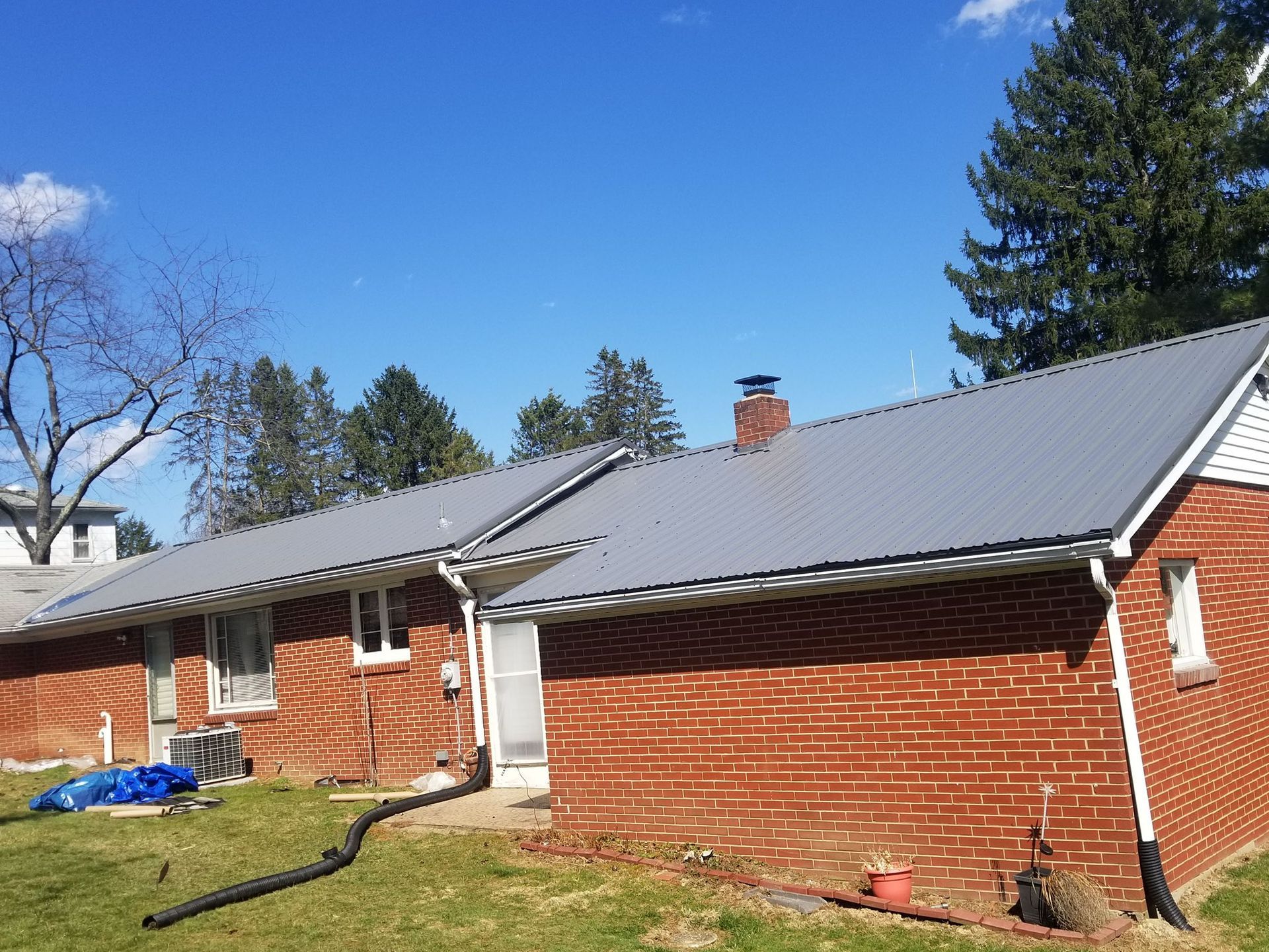 Red brick house with a gray metal roof under a blue sky.