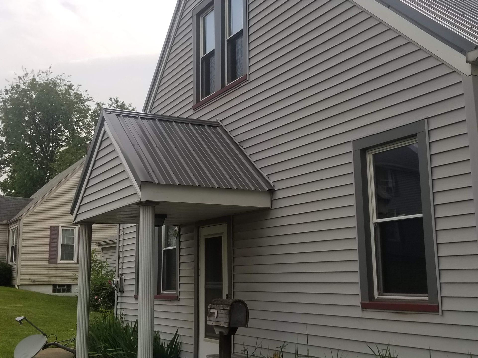 Gray house with metal roof over porch. Light-colored siding, windows with dark trim, mailbox.
