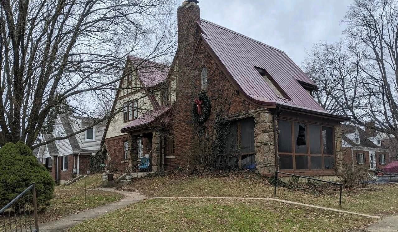 Stone house with red roof, porch, and chimney, covered in ivy, set on a cloudy day.