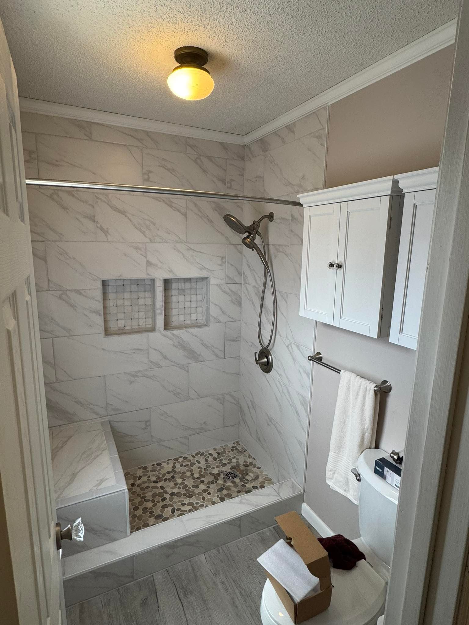 Newly renovated bathroom with marble-look tiles, a shower bench, and white cabinets.