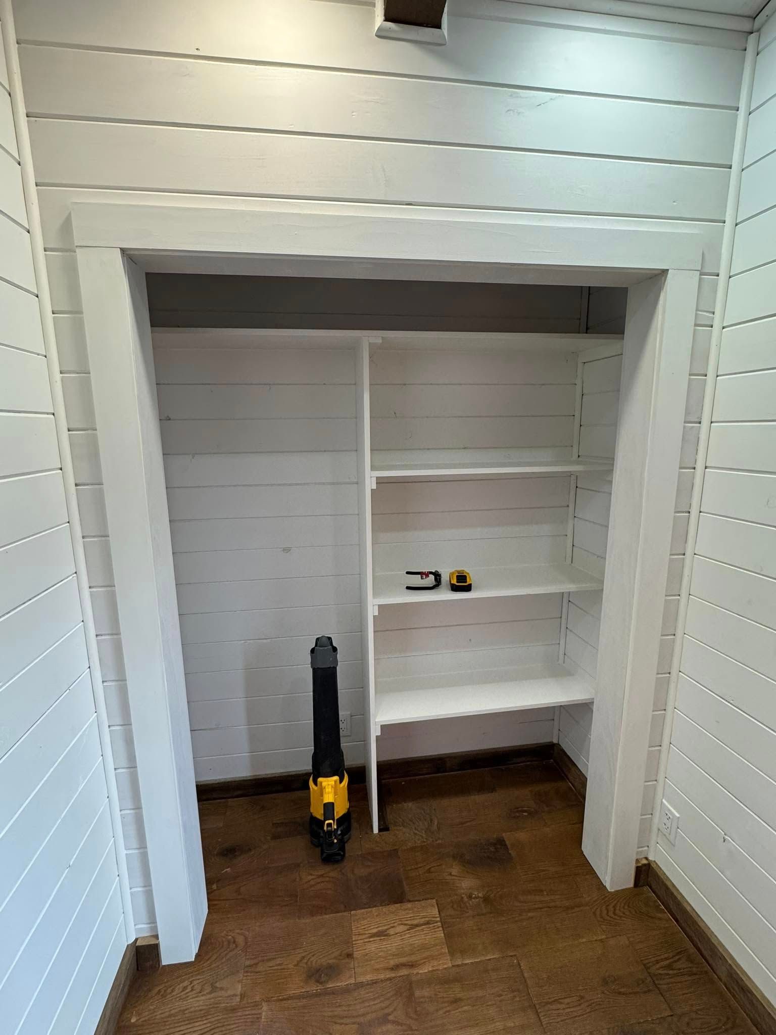 White closet interior with shelves, a door frame, and a nail gun on the floor.