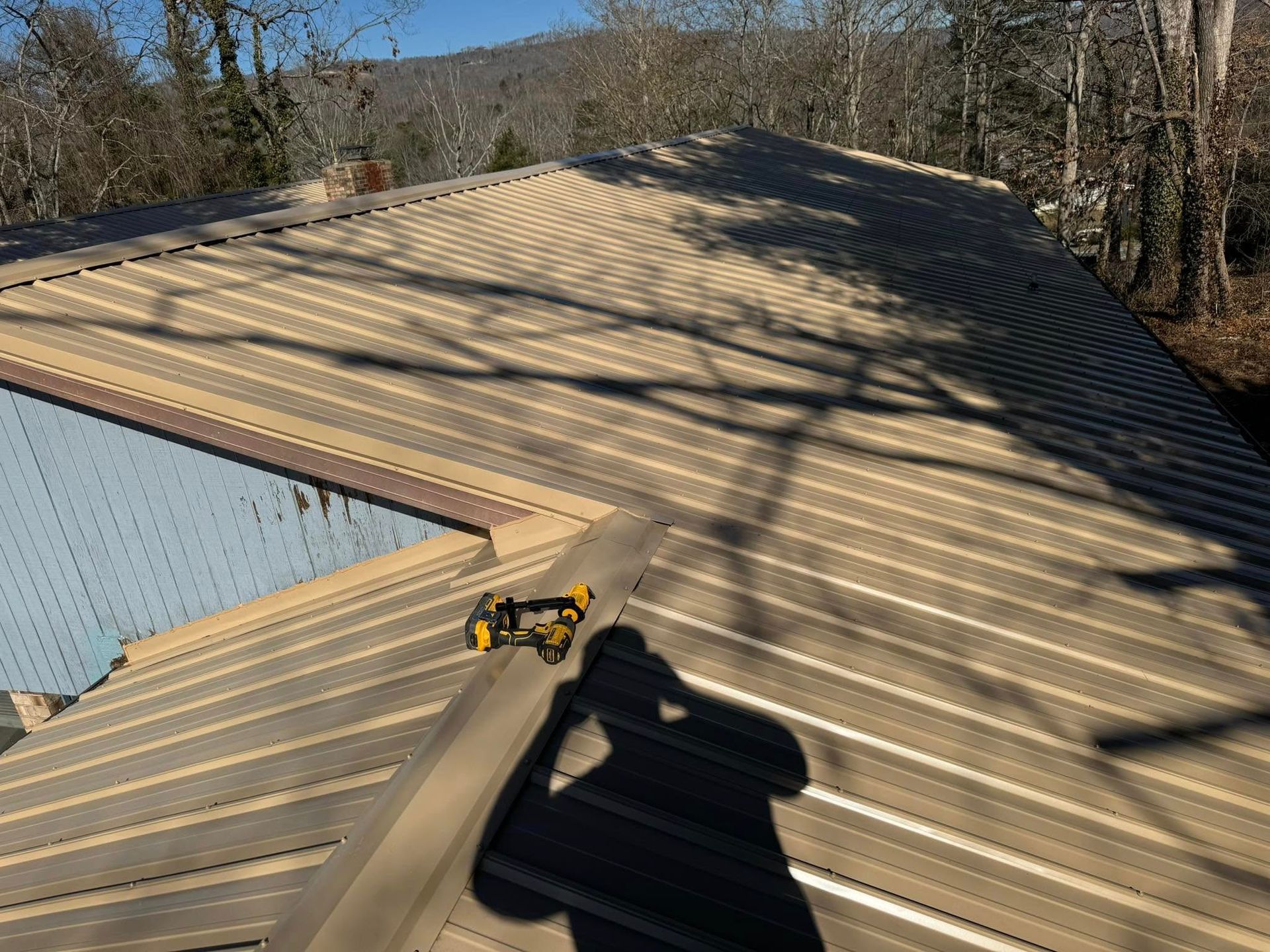 Brown metal roof on a house, with a shadow of a person holding a drill.