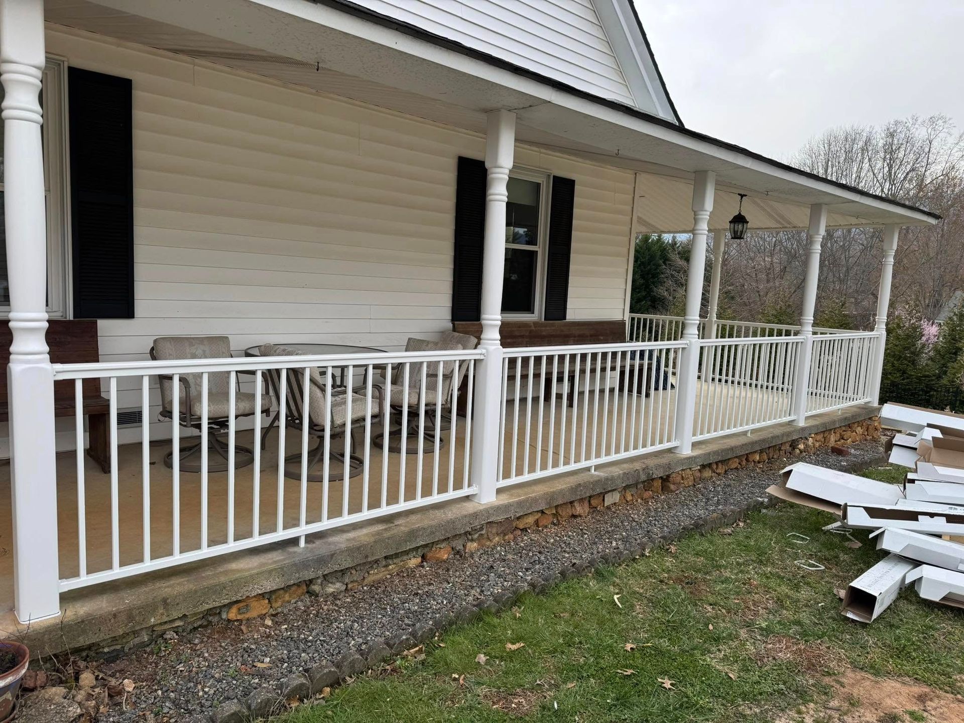 White porch with railing and a house with white siding and black shutters.