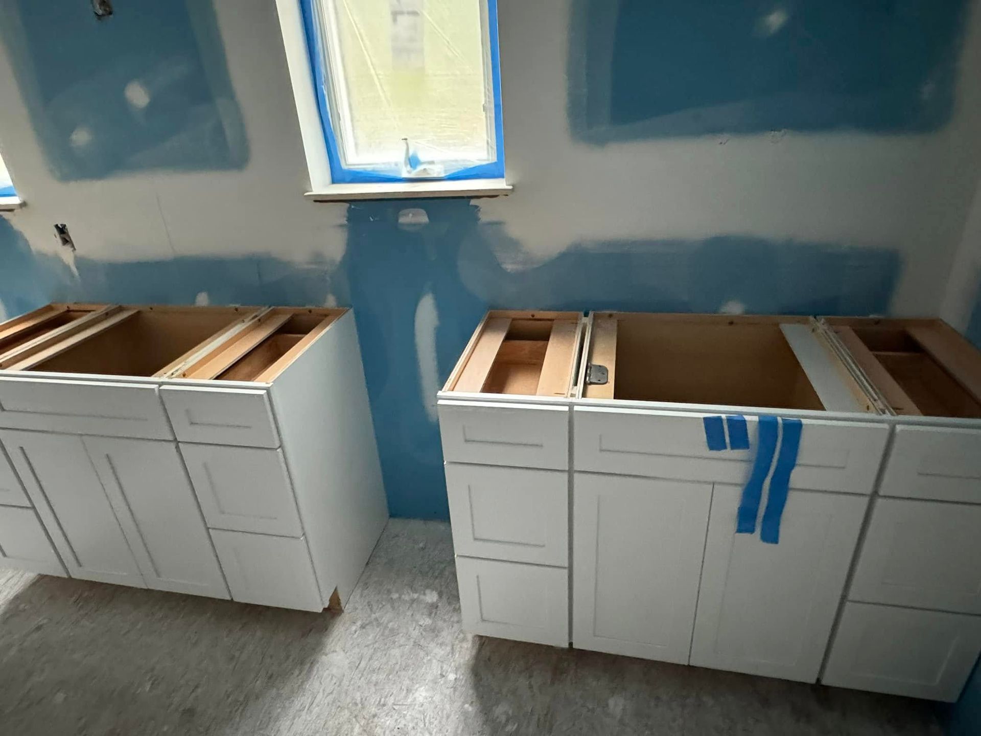 White kitchen cabinets installed against blue drywall, near a window.