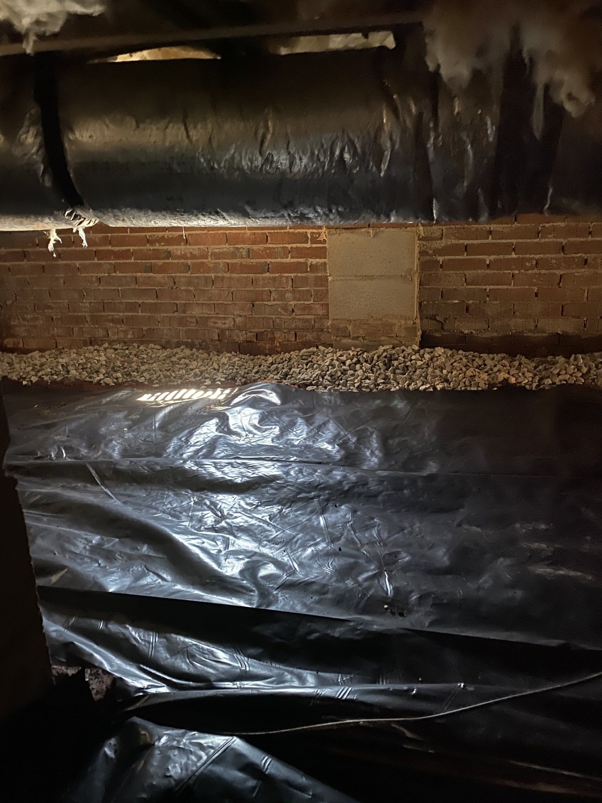 A brick wall is behind a black plastic sheet in a basement.